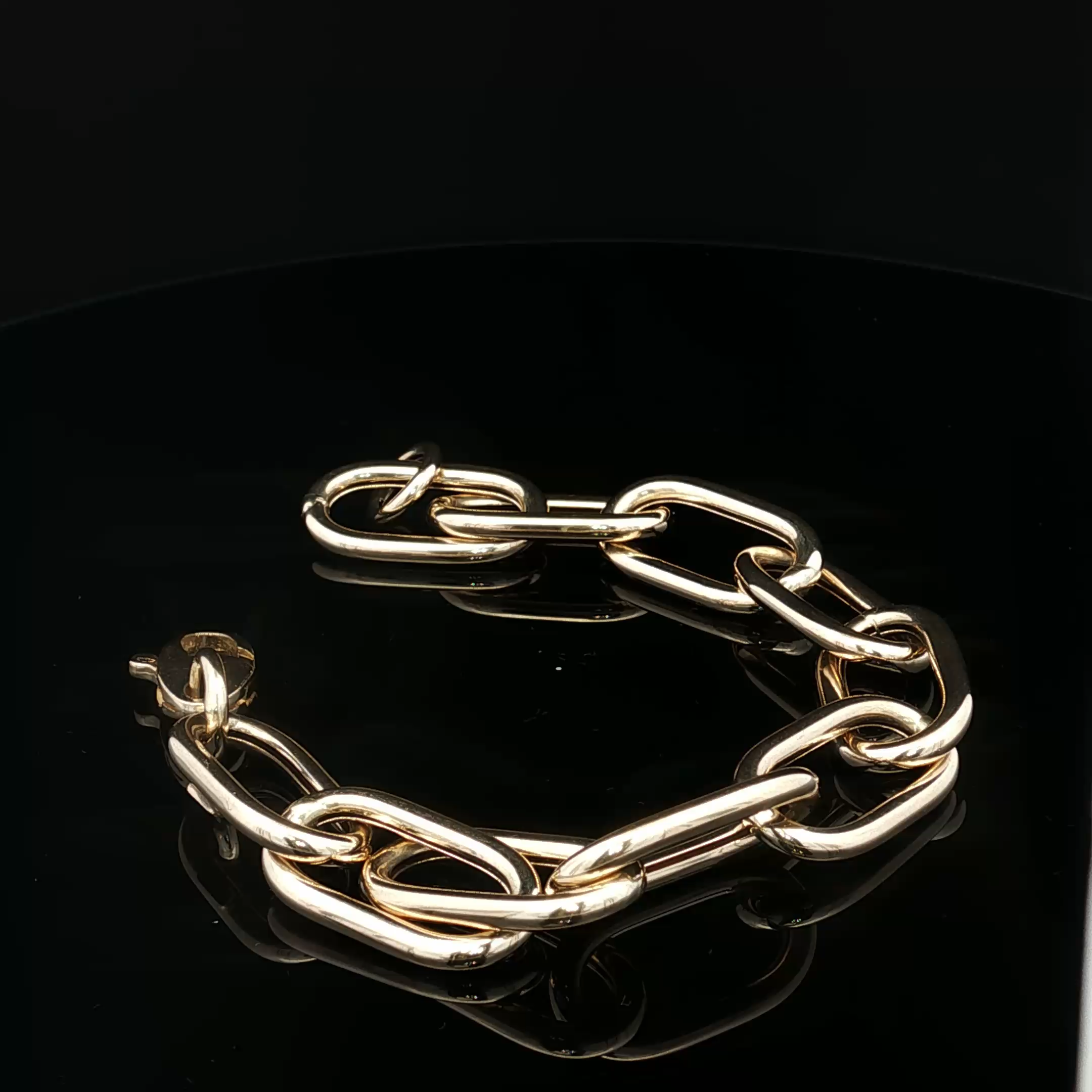 Close-up of gold-colored chain link bracelet against a black background.