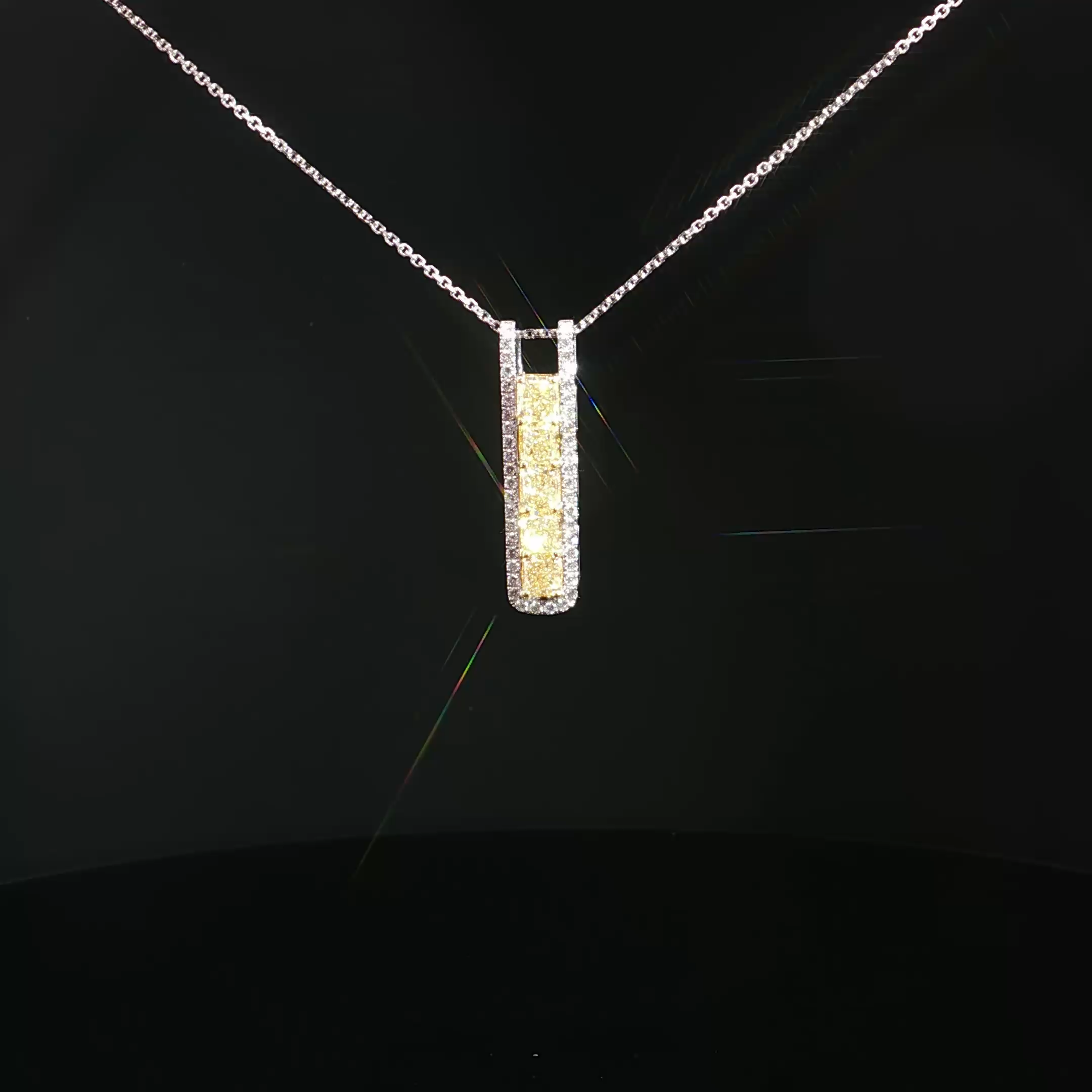 A diamond necklace with a rectangular pendant hanging from a chain, displayed against a black background.