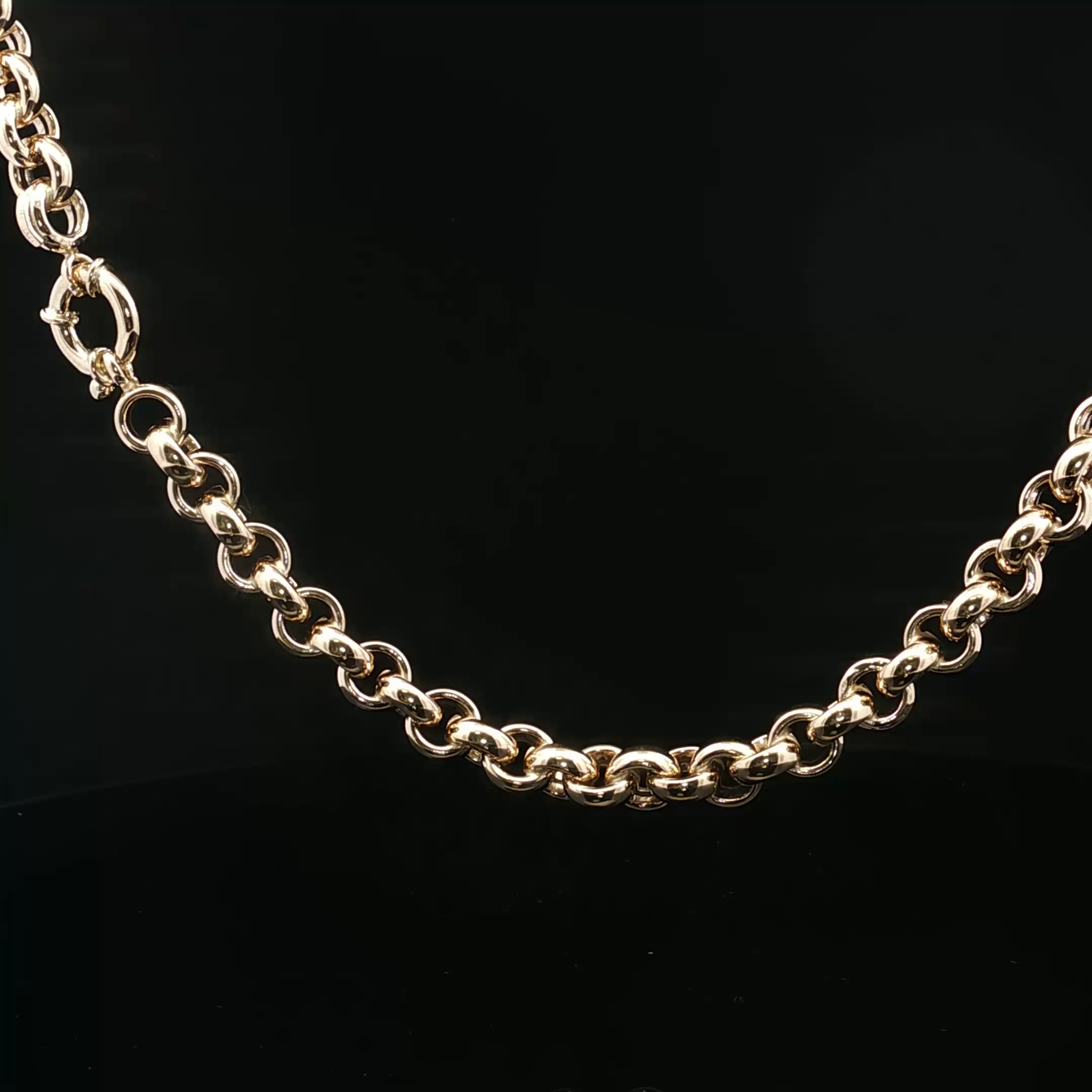 Close-up of a gold chain necklace with interlocking links on a black background.