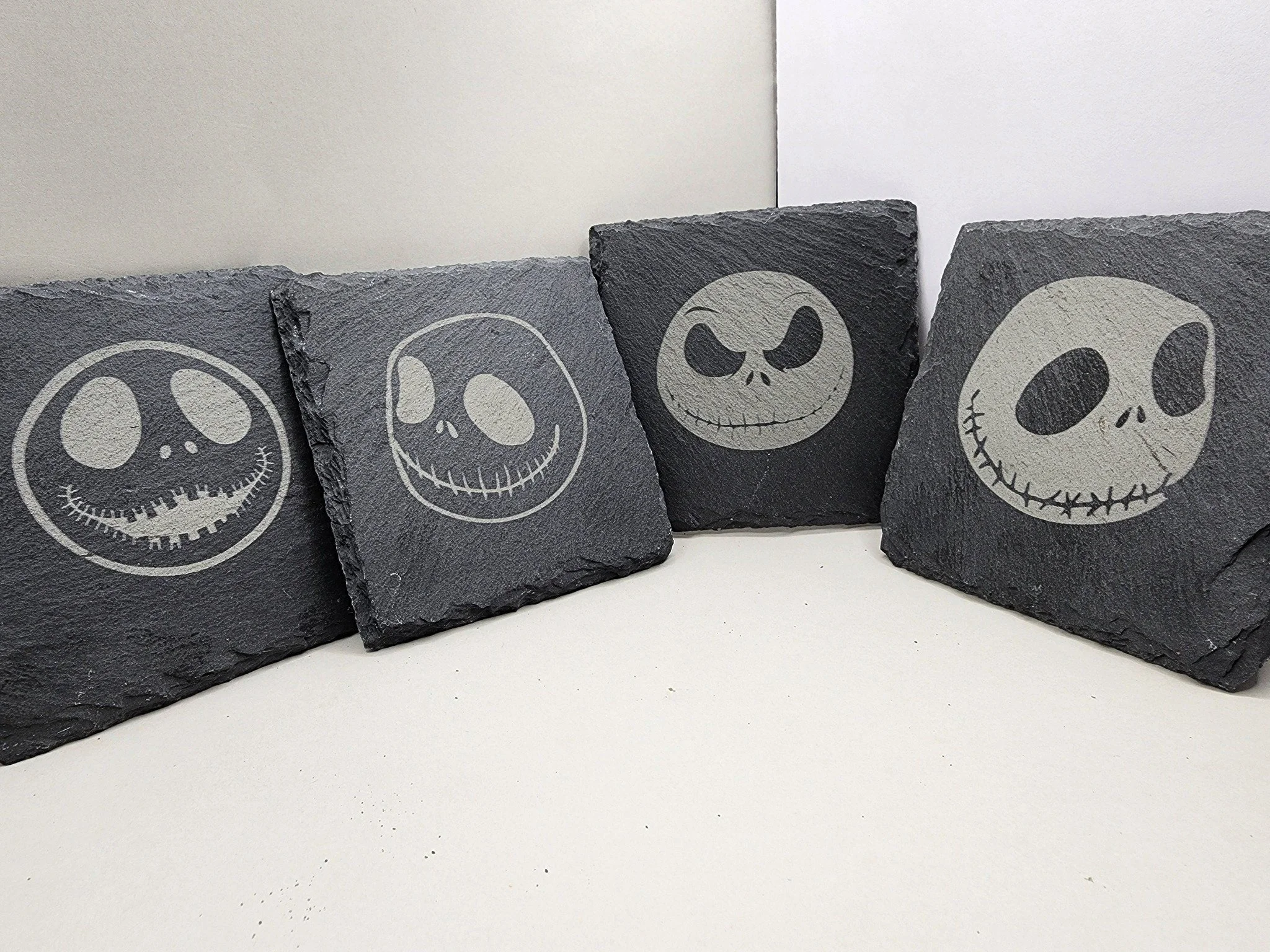 Four black slate tiles with white ghostly skull faces etched into them, each with different facial expressions.