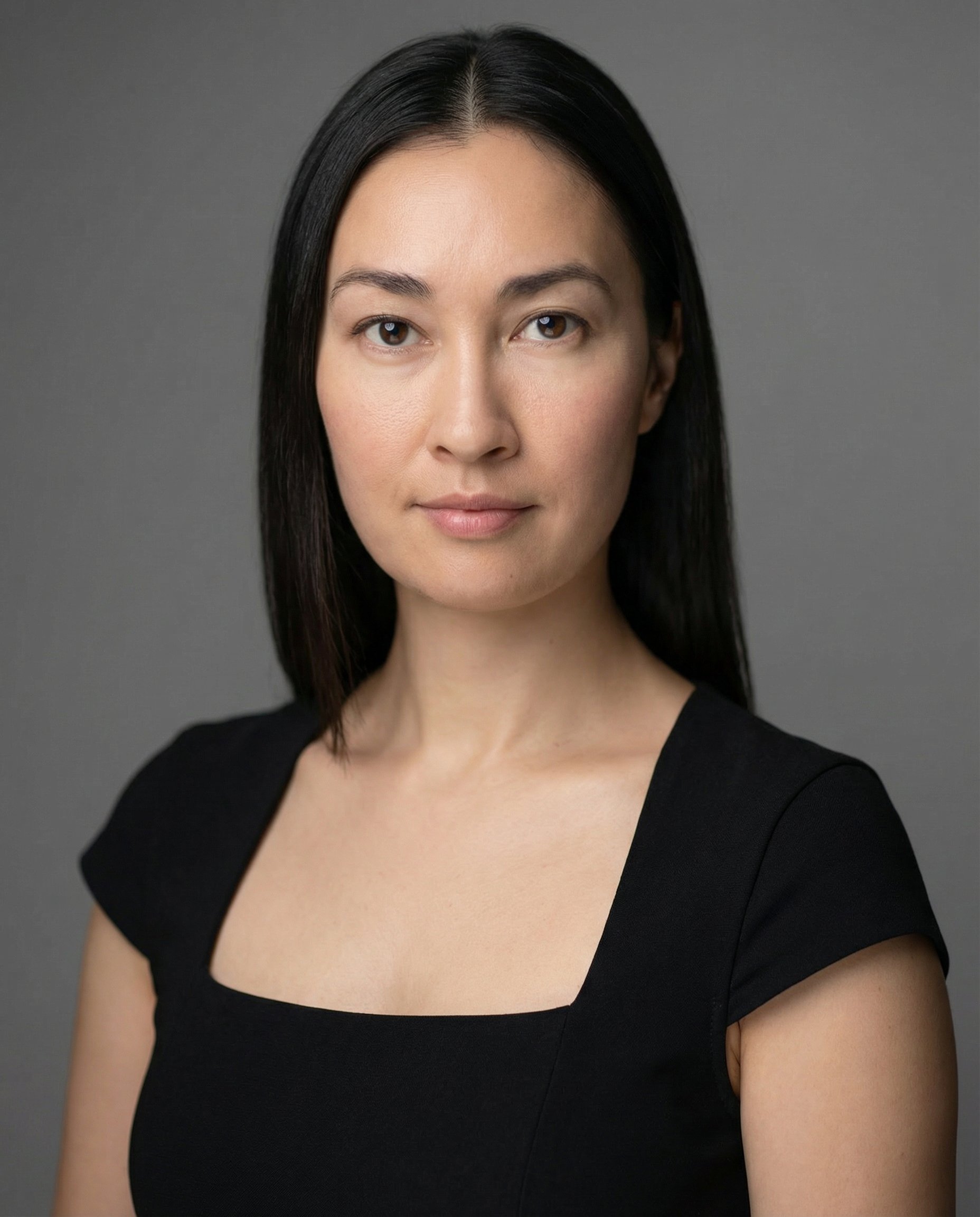 Portrait of a woman with straight black hair, wearing a black top, against a gray background.