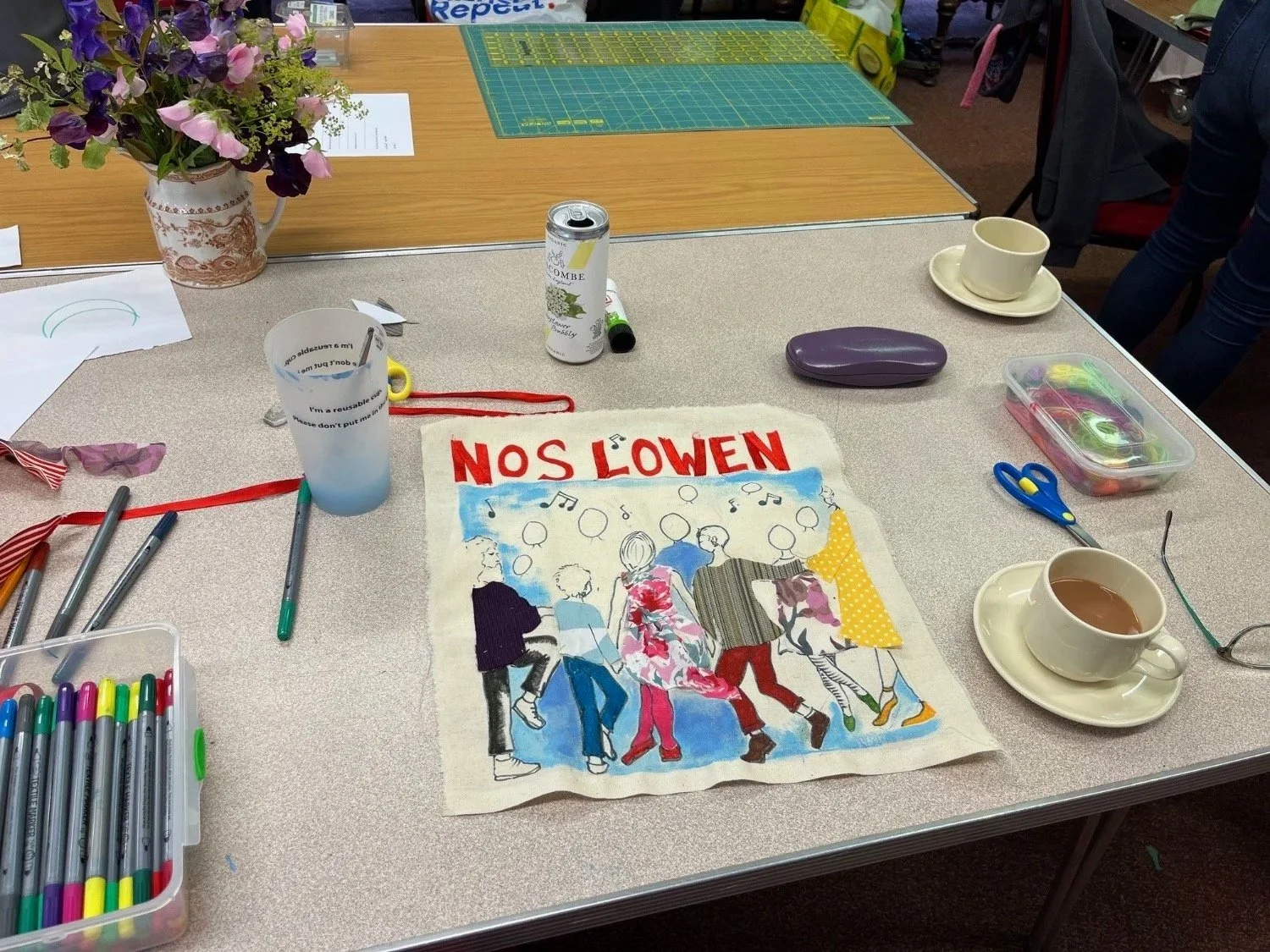 A table covered in craft materials and a fabric panel depicting people dancing. 
