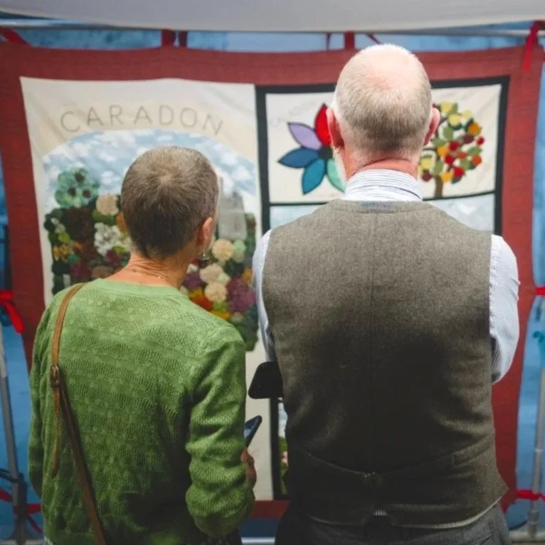 Two visitors view panels depicting stories about Cornwall inside Story Shelter by Bec Applebee.
