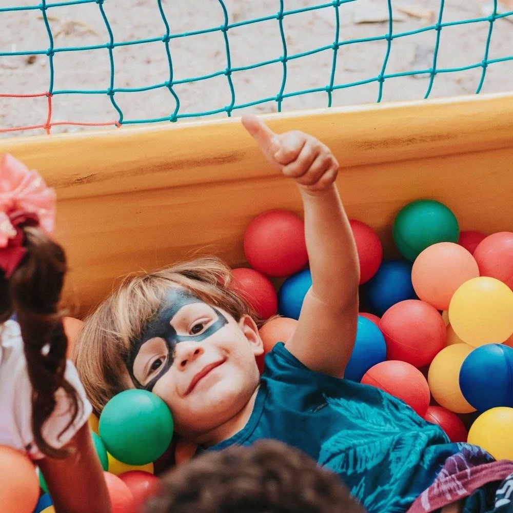 A boy in a black masks plays in a ball pit.