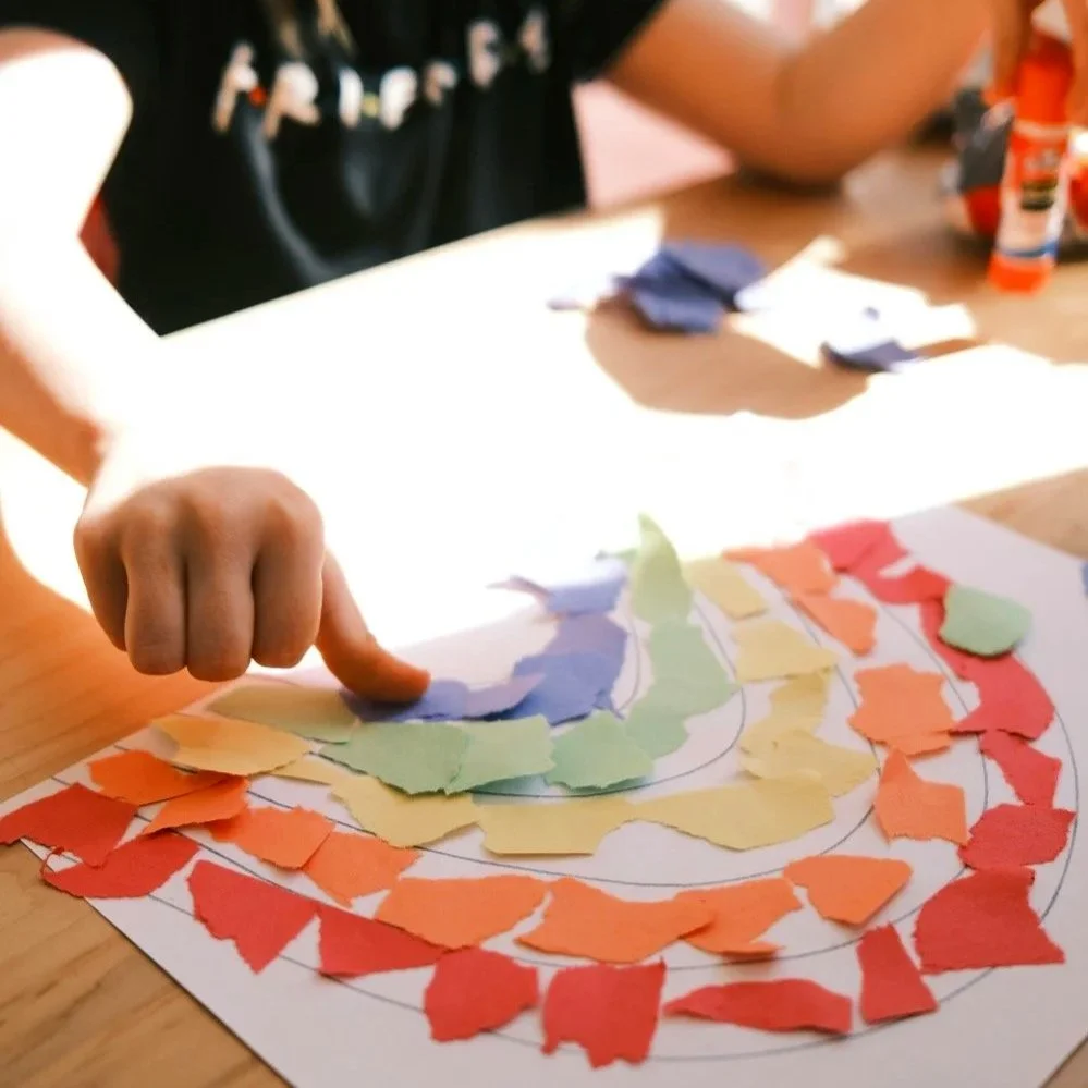 A child makes a rainbow collage from coloured paper.