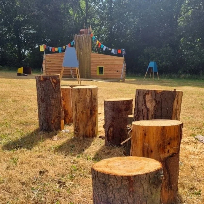 A series of wood stepping stumps in front of a Play Pavilion at Let's Play.