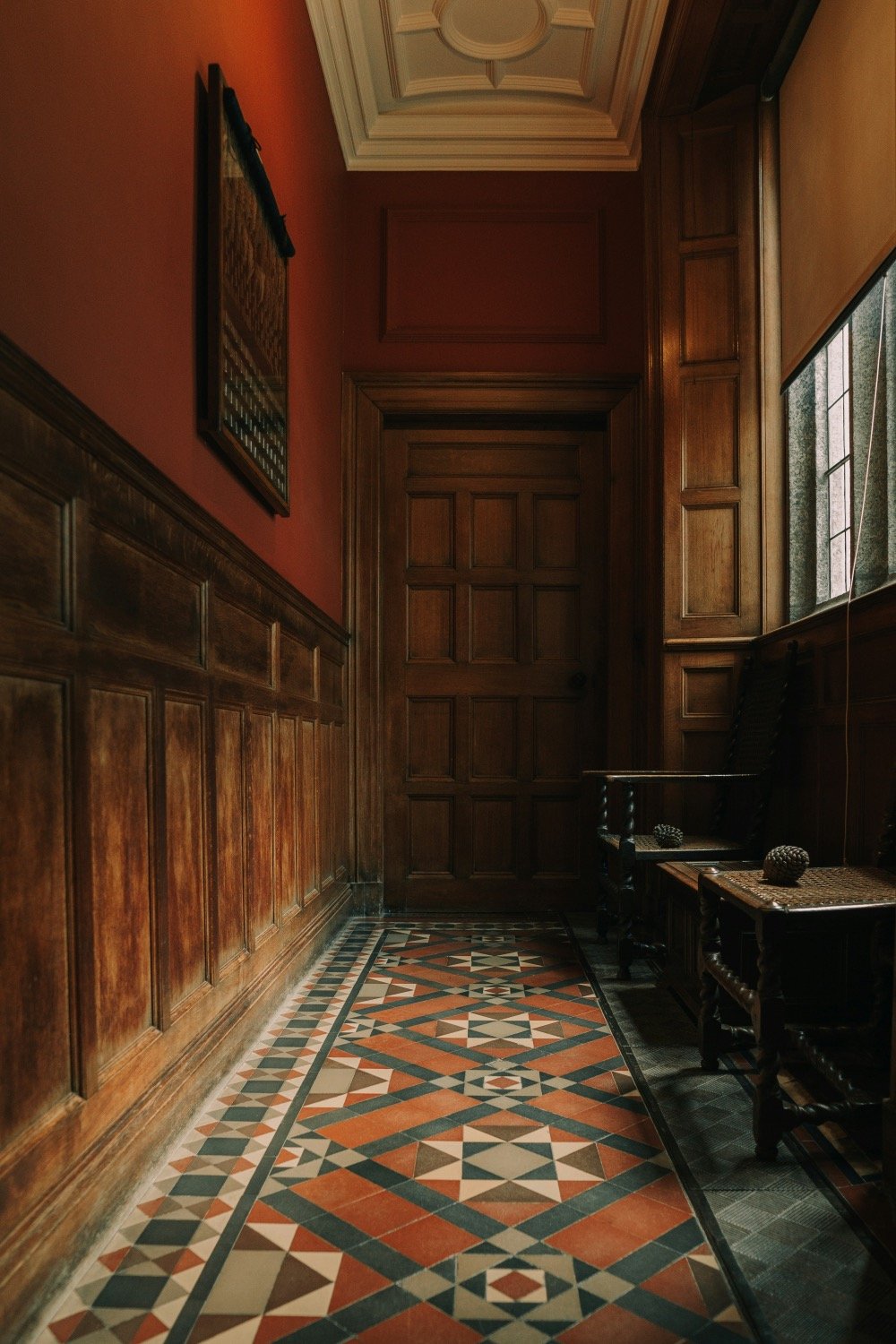 A red wood-panelled hallway with a tiled mosaic floor in Lanhydrock house in Cornwall.