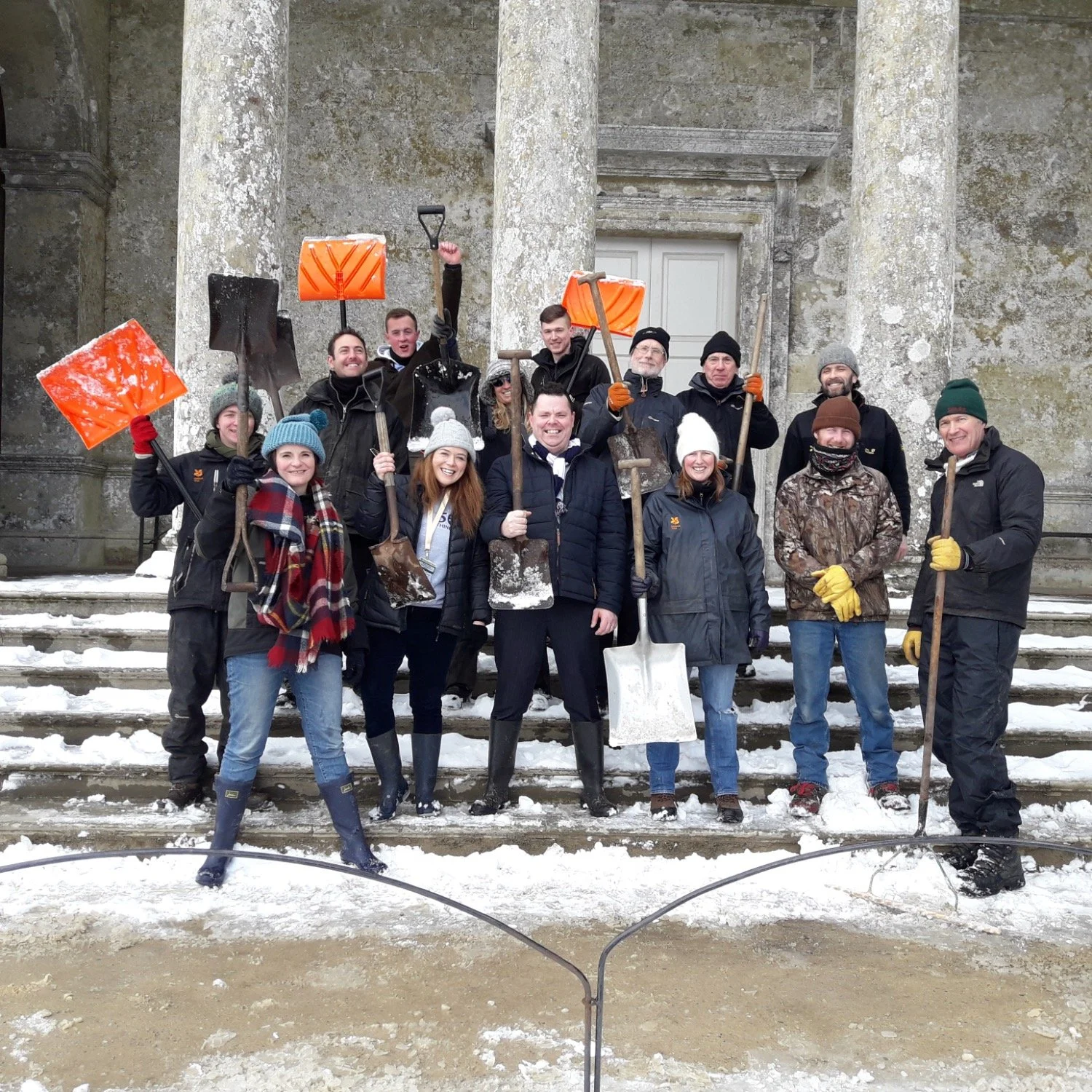 The Stourhead team stand on the steps of the Pantheon cheering while holding snow shovels.