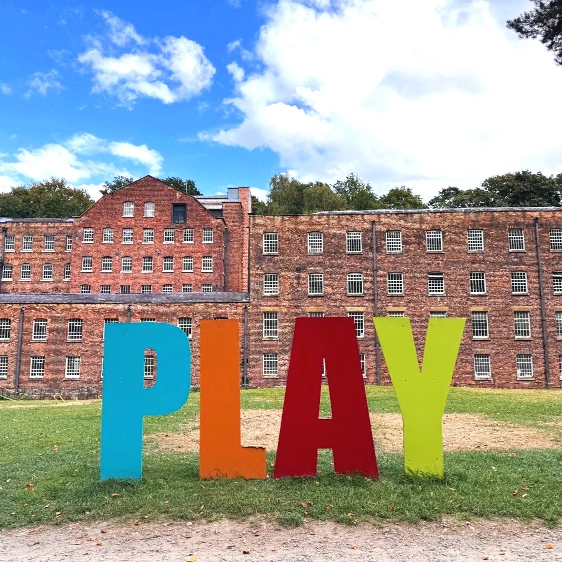 Large coloured letters spell the word 'Play' in front of Quarry Bank Mill.