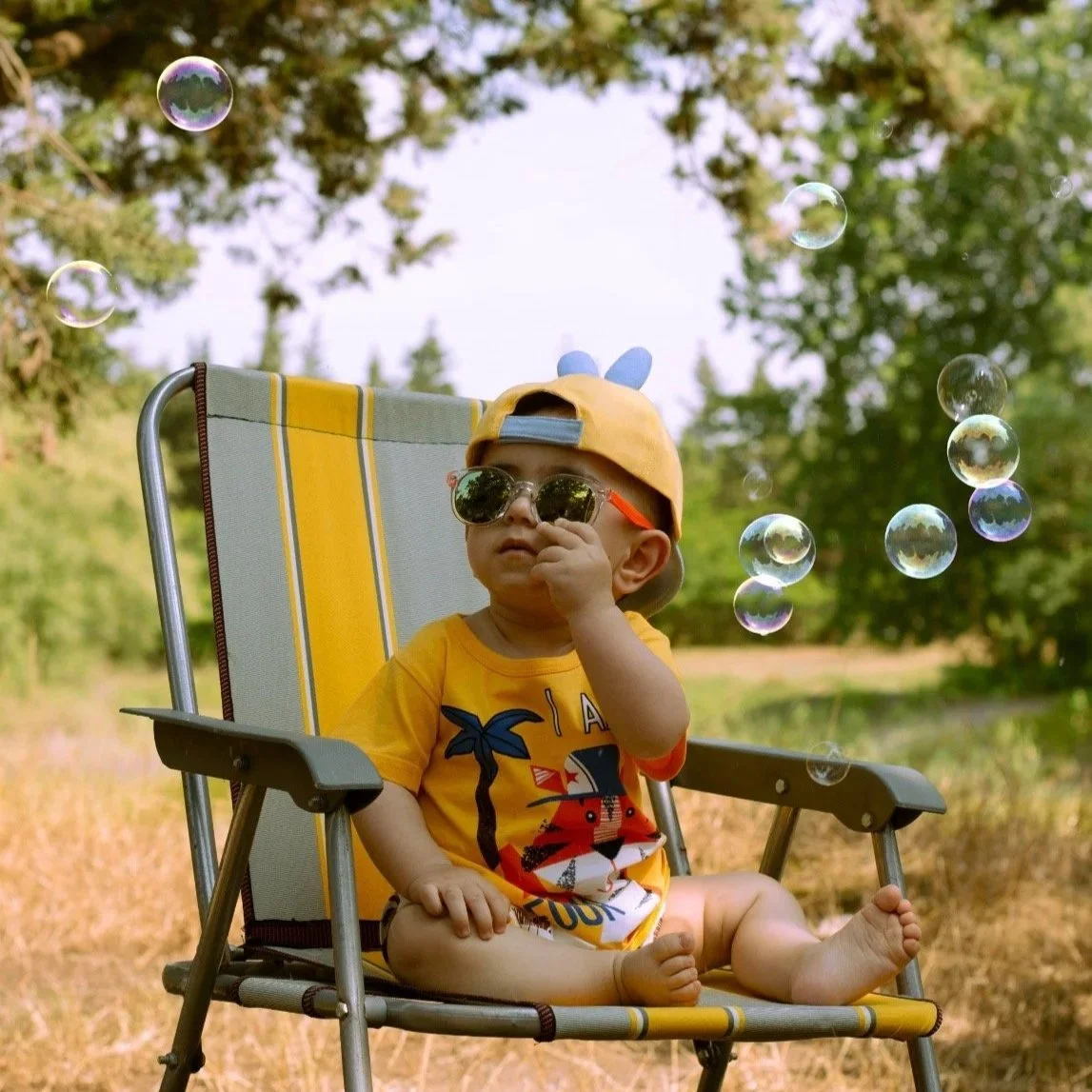 A toddler in a yellow t-shirt and sunglasses plays with bubbles.