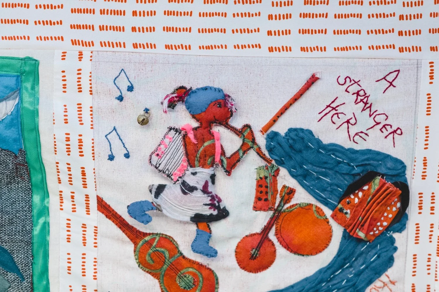 A fabric panel depicts a figure playing an instrument with a caption reading 'A stranger here'.