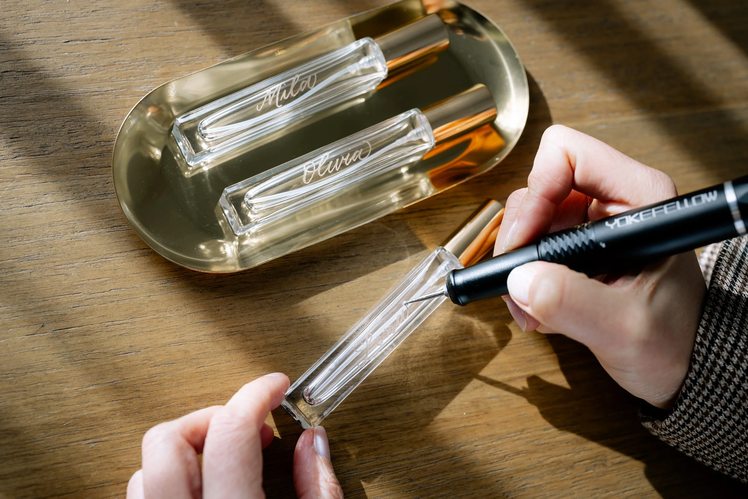 Person filling a diffuser with oil labeled 'Miala' using a black marker, on a wooden surface with a silver tray holding two glass bottles.