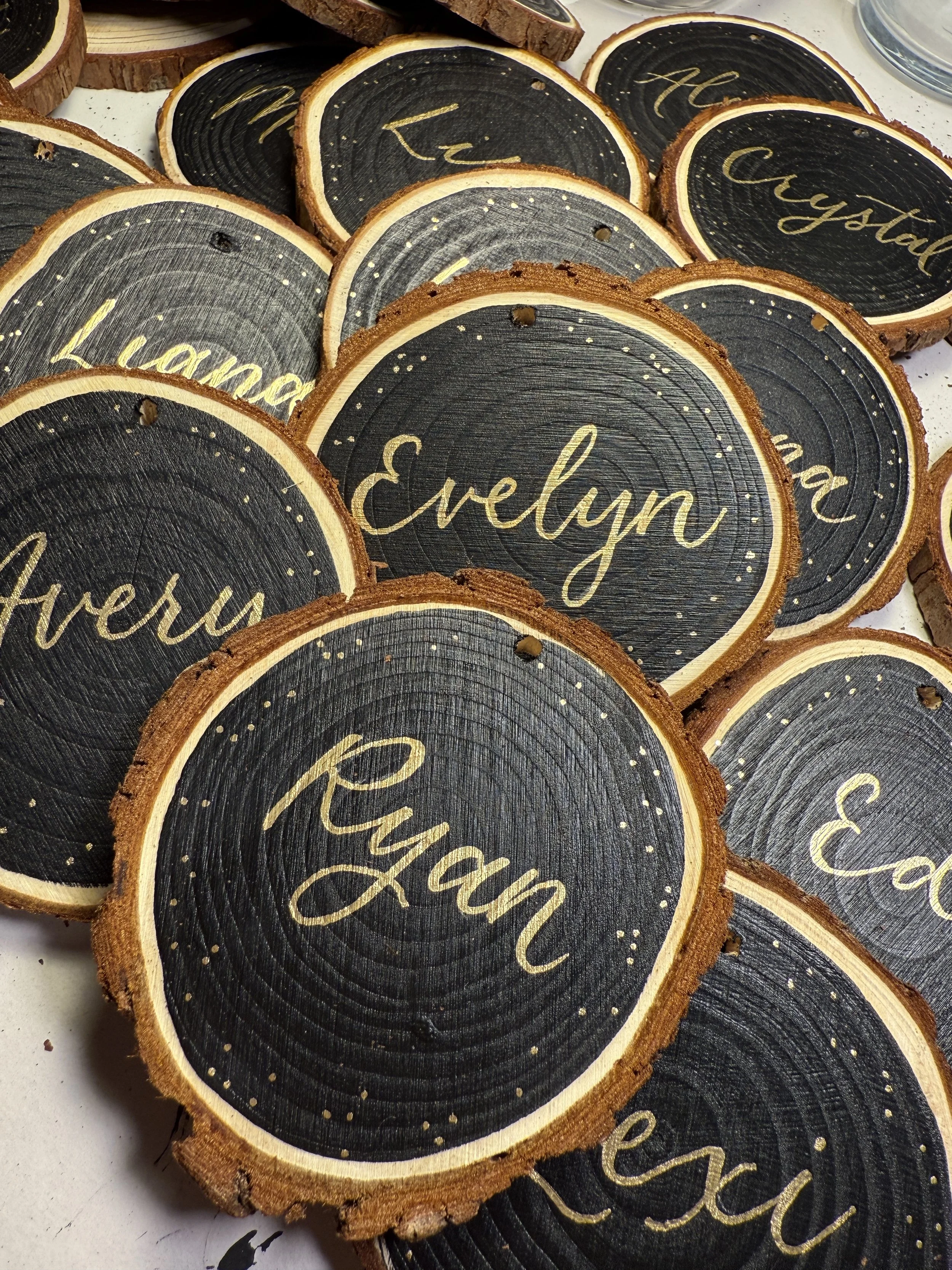 Wood slices with black painted centers and gold script names, including Evelyn and Revan, arranged on a surface.