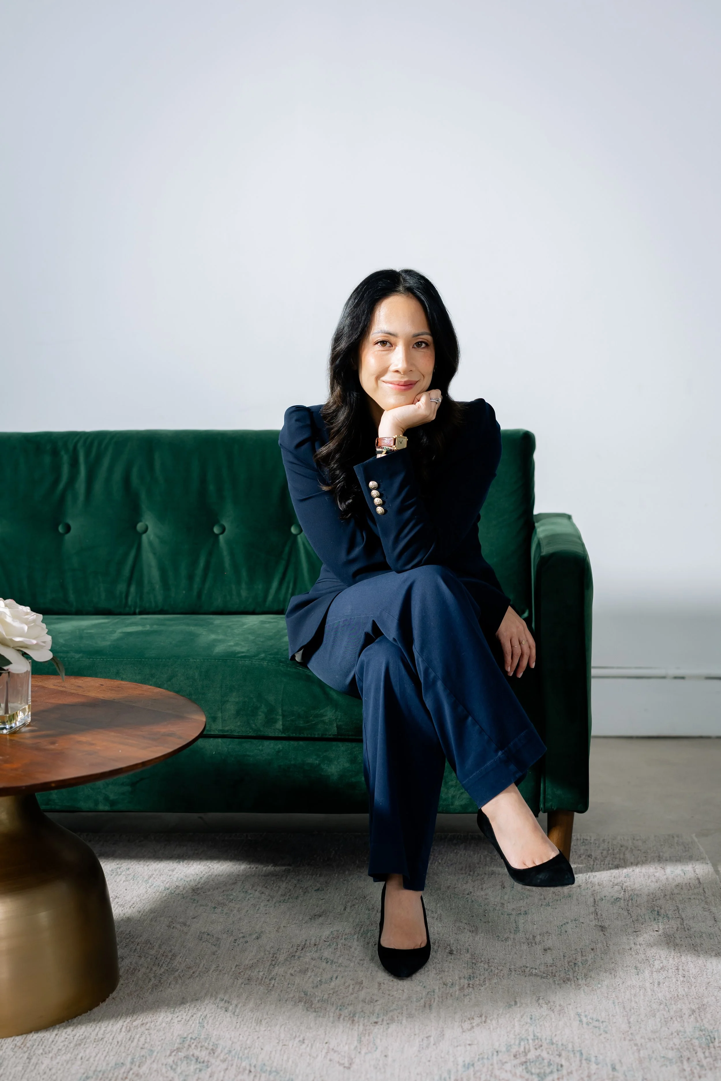 Kaity Kwock of kwk creative studio, sitting on a green velvet sofa with her head perched up by her left hand. Kaity Kwock is a calligrapher and engraver serving the New York and New Jersey areas.