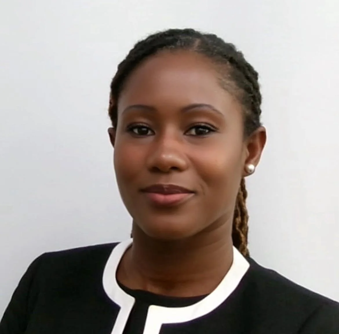Close-up portrait of a woman with dark skin, wearing earrings and a black top with white trim, against a plain white background.
