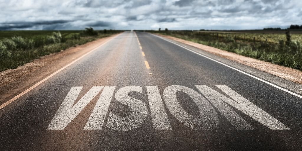 An empty open road stretching into the distance with the word "VISION" painted on the asphalt in large white letters.