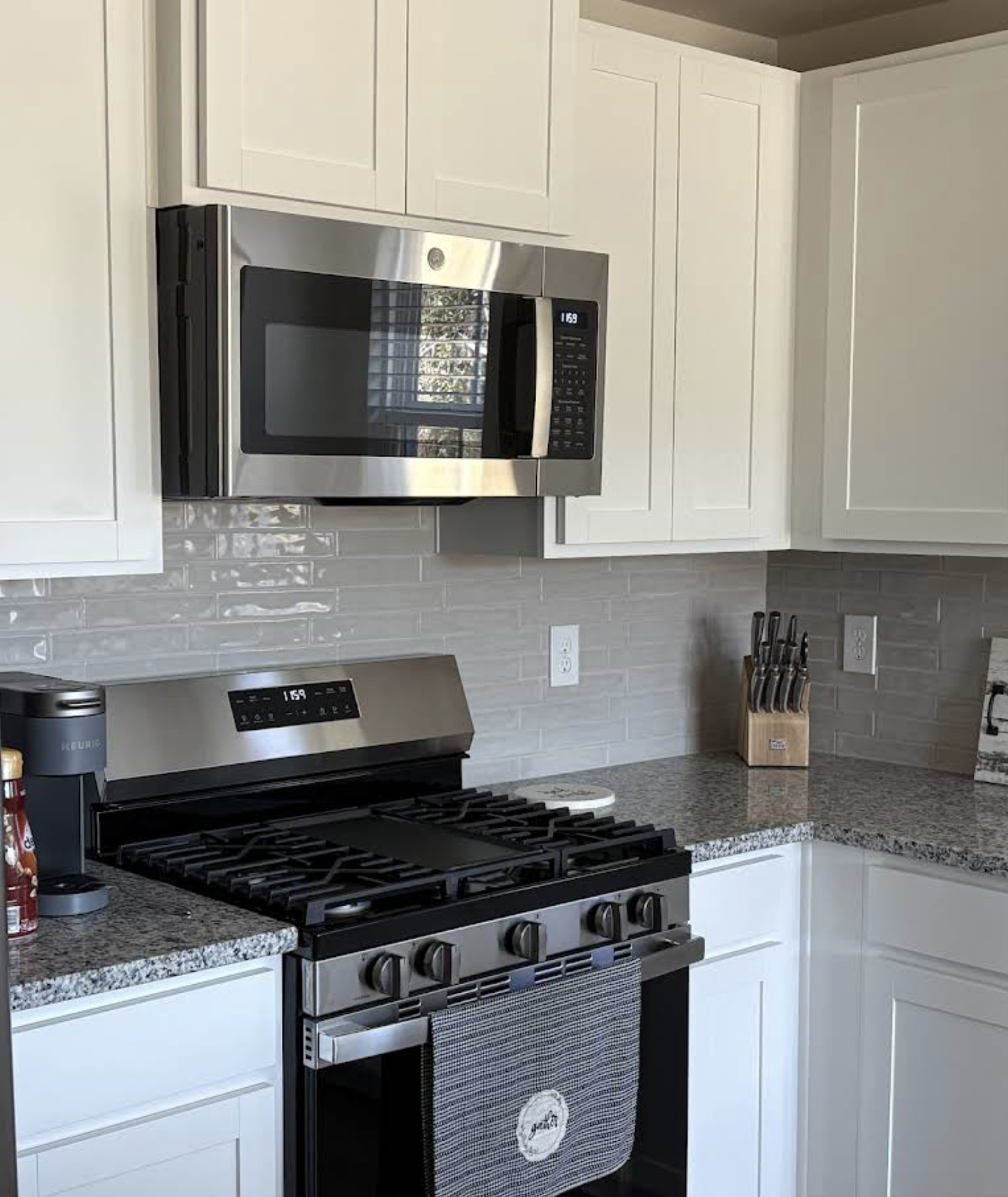 Kitchen with white cabinets, granite countertops, stainless steel microwave above stove, gas stove, knife block, and electrical outlets.