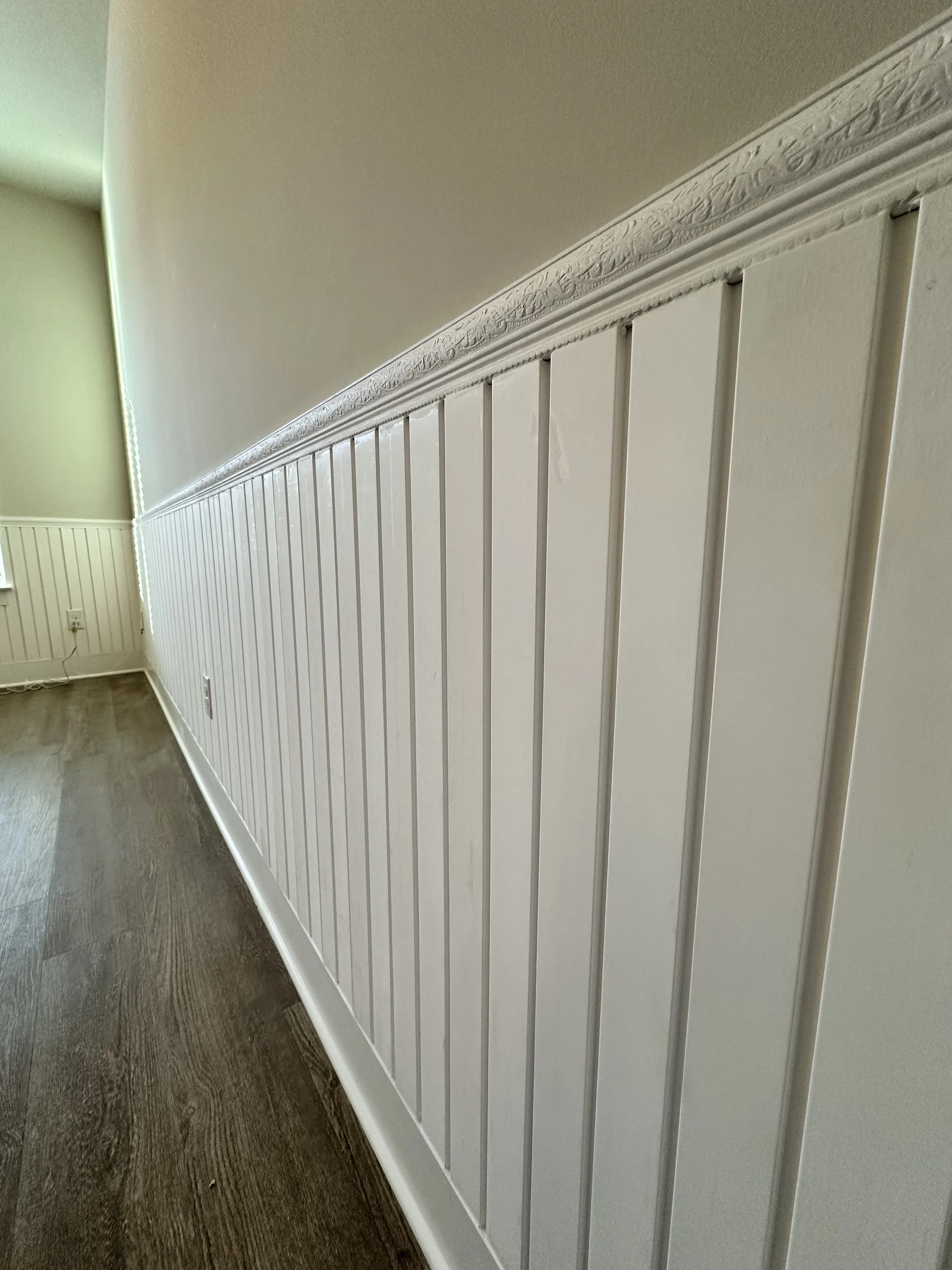 Interior wall with decorative molding and beadboard paneling in a room with hardwood floors