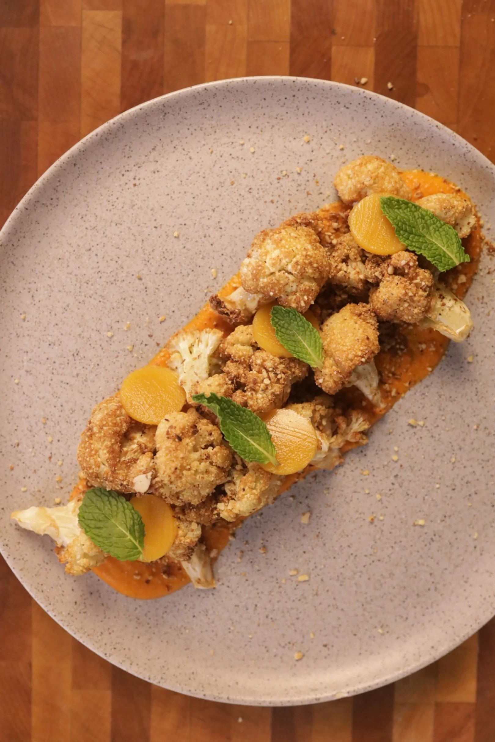 Fried cauliflower bites with yellow pickled peppers and fresh mint leaves on a speckled ceramic plate.