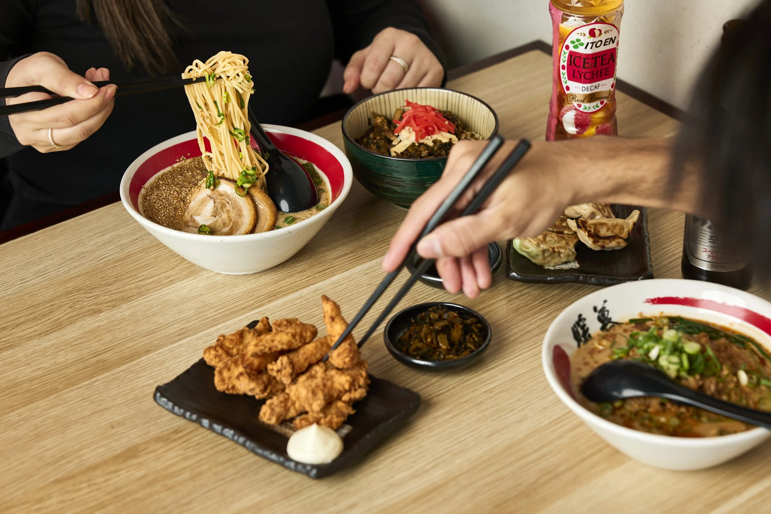 Menschen essen japanisches Essen, einschließlich Ramen, Gyoza und frittiertes Hähnchen, auf einem Holztisch.