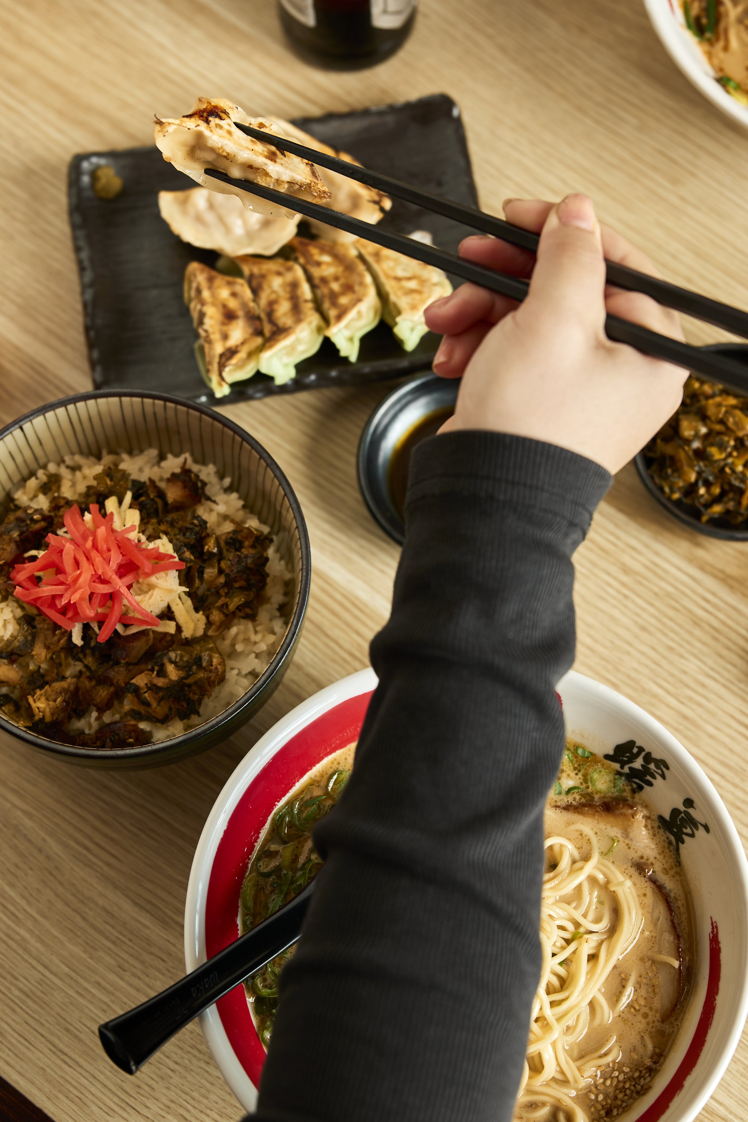 Person, die mit Essstäbchen eine Dumpling hält, auf einem Sushi-Teller