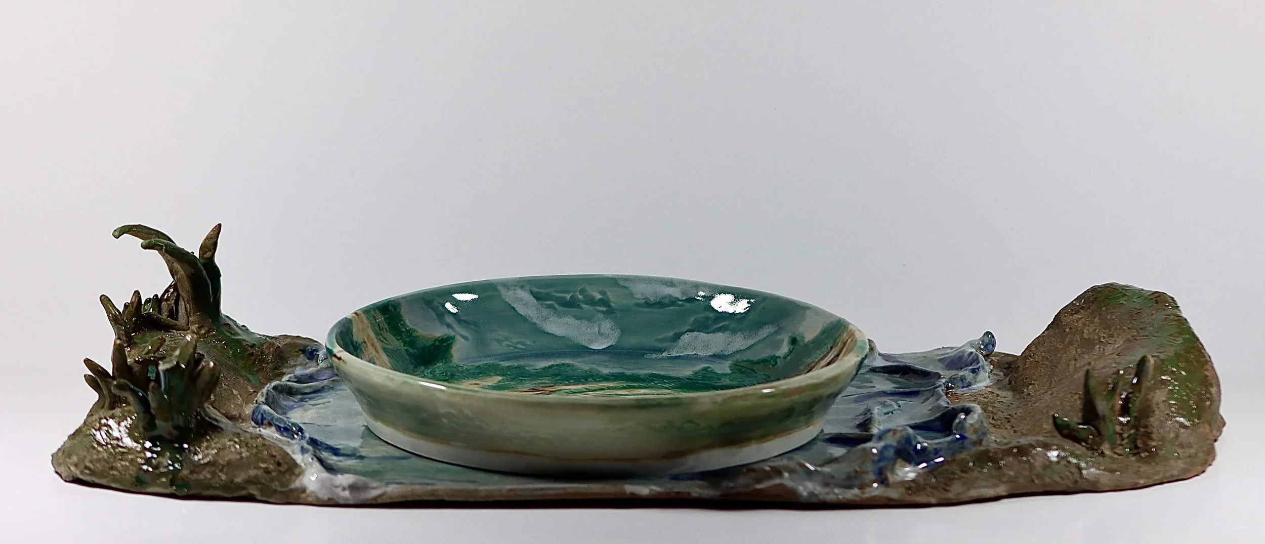 "My Rushing Waves of Culture II", 2026. Glazed Red Stoneware and Porcelain. 10.75" x 8.25" inches.

 Part of a series . A ceramic plate with a tray in the form of a lake showcasing my mother in San Jose, Peru cradling a sheep.