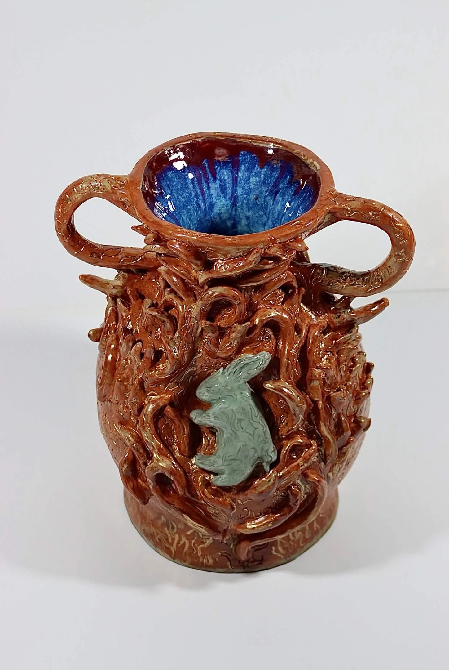 "Frail Spirit Burning Brighter", 2026. Glazed Red Stoneware with porcelain slip and acrylic paint. 9" x 16" inches. A ceramic vessel entails a docile soul in the form of a rabbit spreading its luminous flames. 
