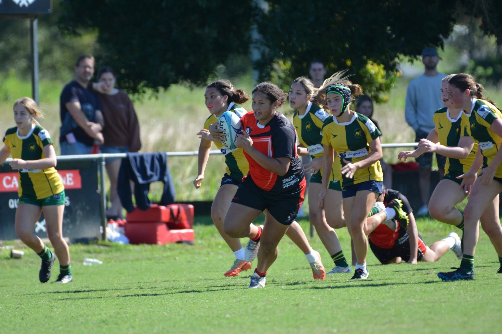 Rugby players in yellow and green uniforms running with the ball during a game on a grassy field.