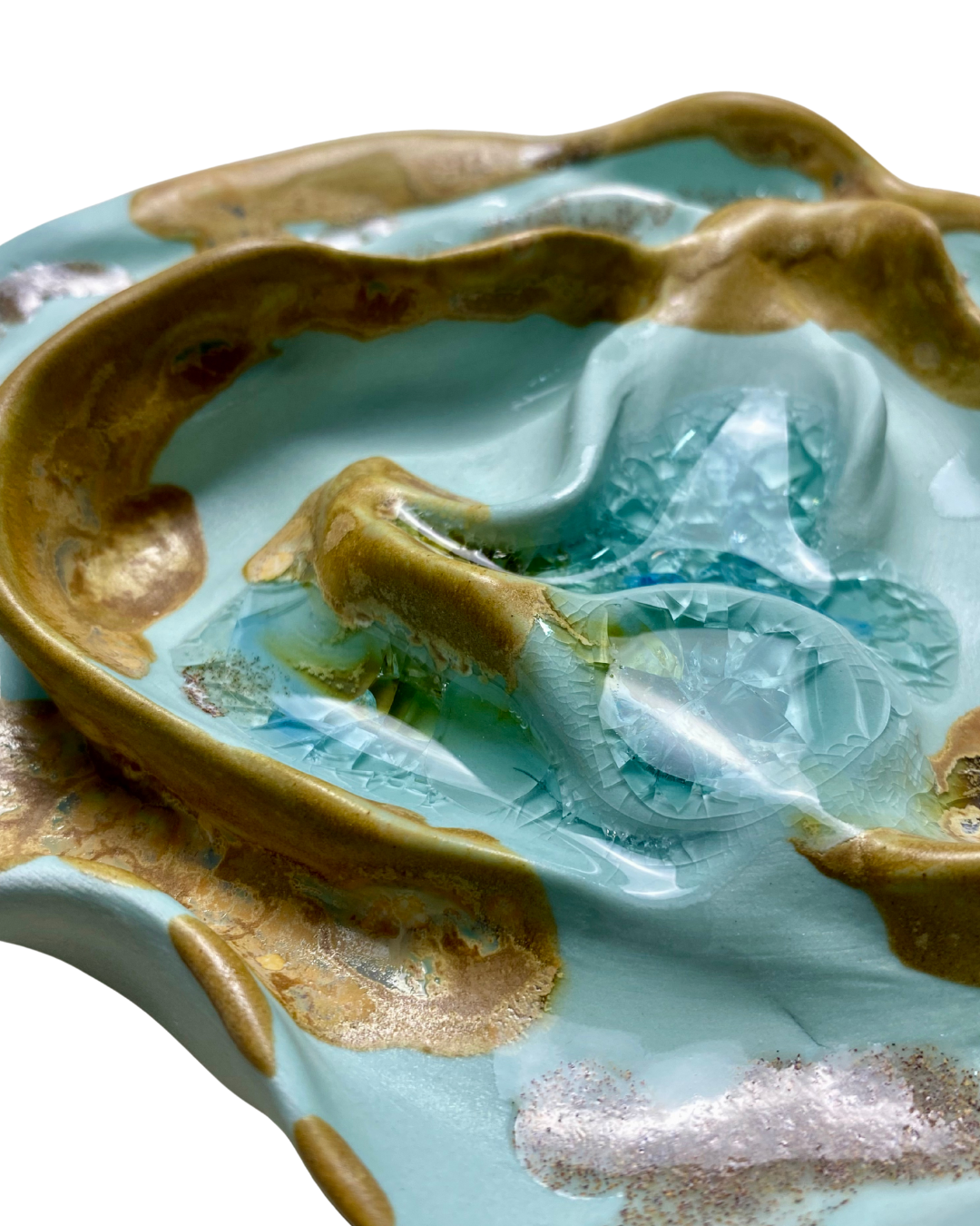 Detalle de una escultura de cerámica con tonos azules y dorados, mostrando texturas y acabados metálicos en la superficie.