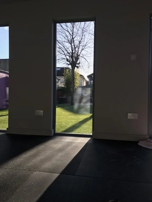 View through a glass door showing a backyard with green grass, a large leafless tree, and neighboring houses.