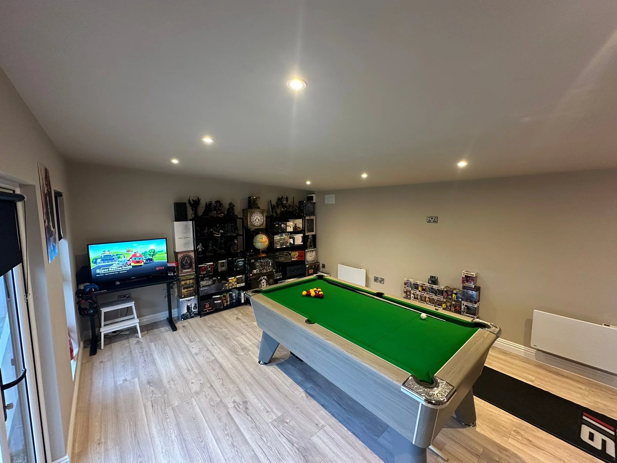 A room with a pool table, TV on a stand, and shelves filled with collectibles and figurines.