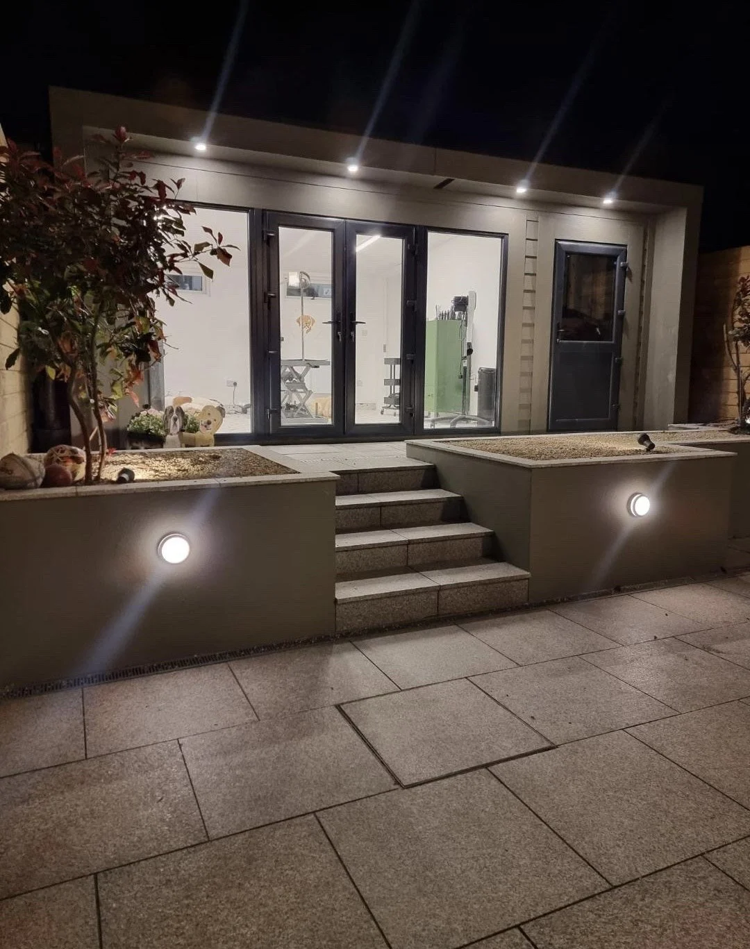 Night view of a house exterior with a porch, steps leading to glass sliding doors, and outdoor lighting