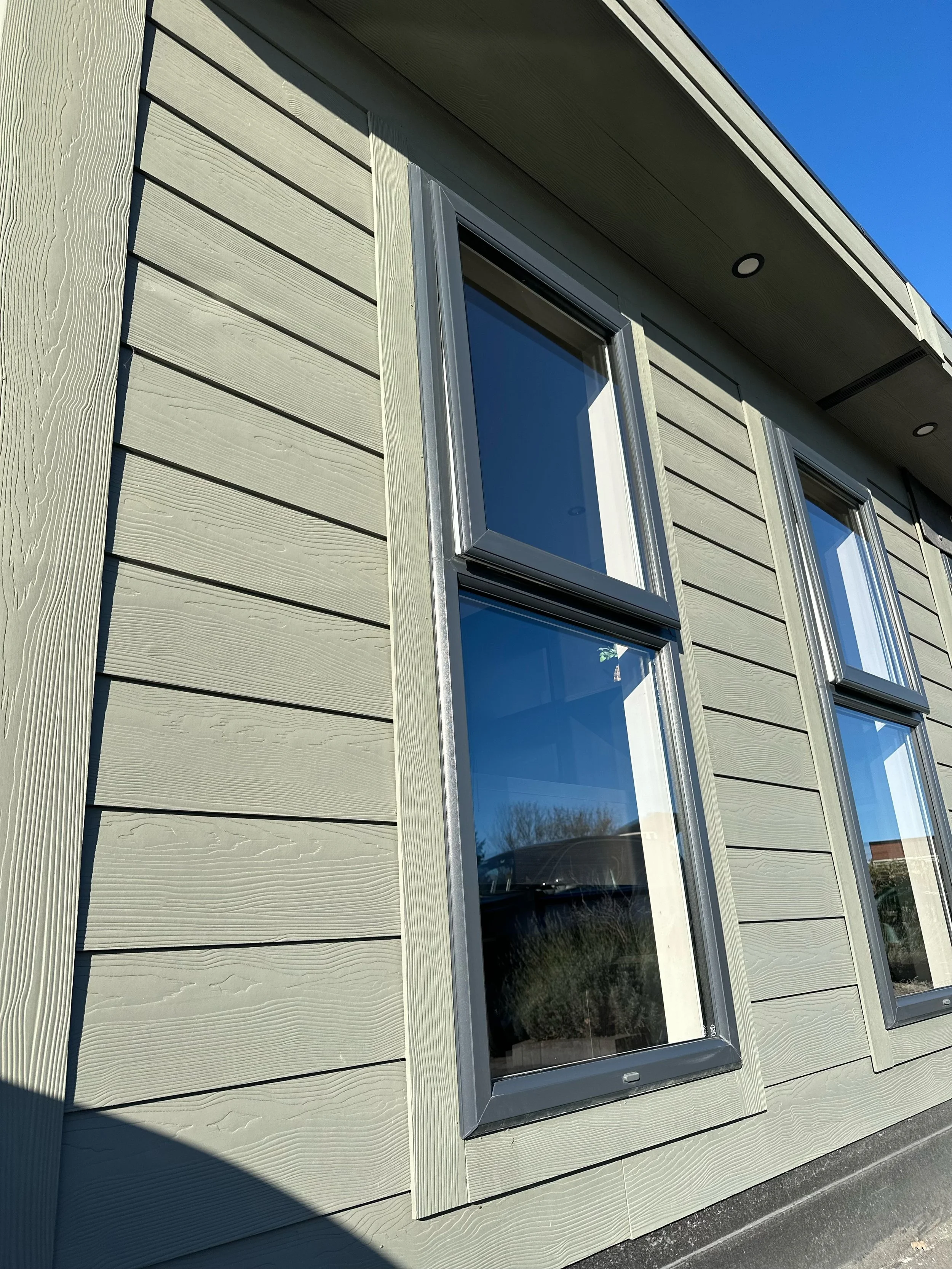 Close-up of the exterior wall of a modern house with horizontal siding and three large windows, under a clear blue sky.
