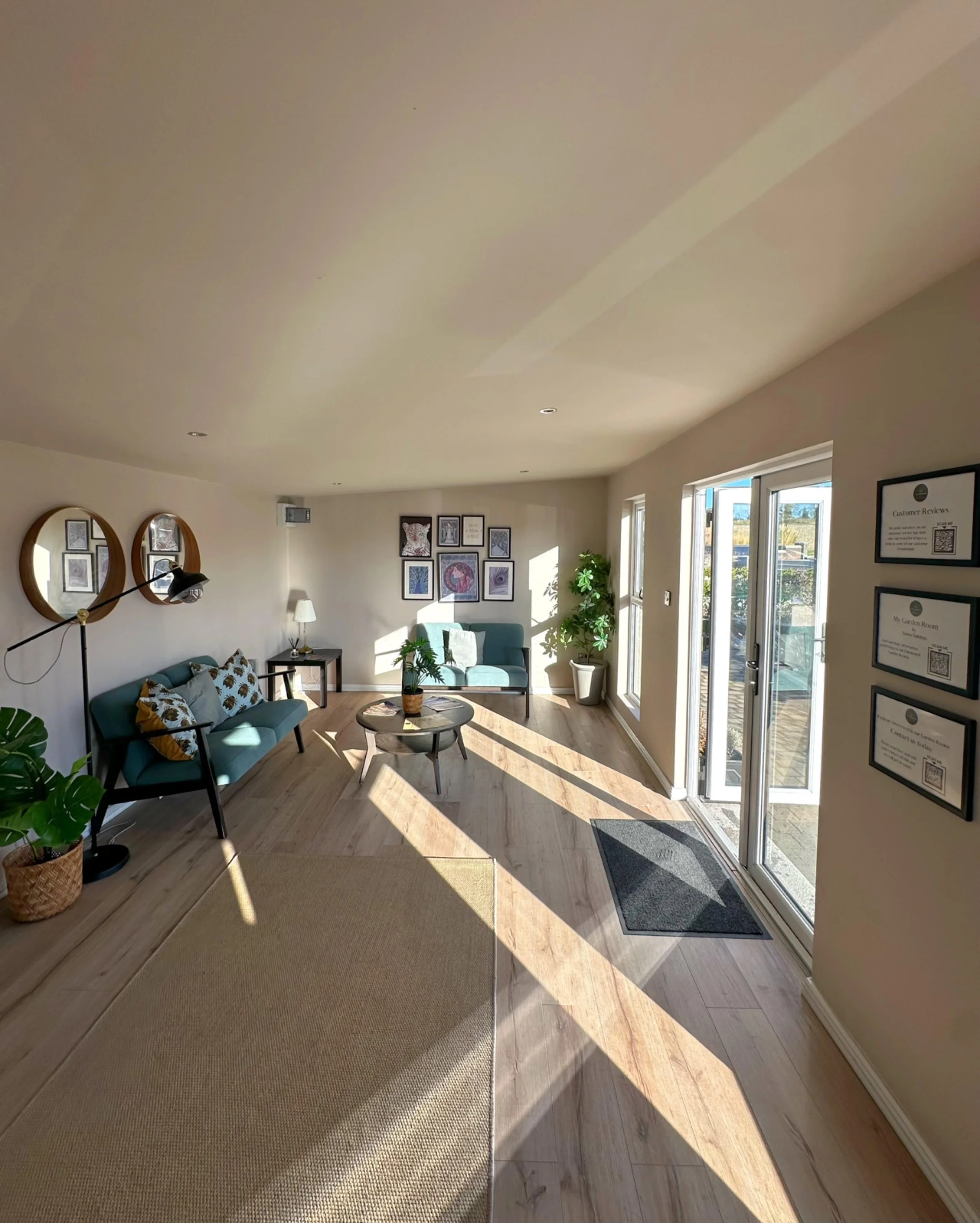 Sunlit living room with blue chairs, wall art, potted plants, and a glass sliding door leading outside.