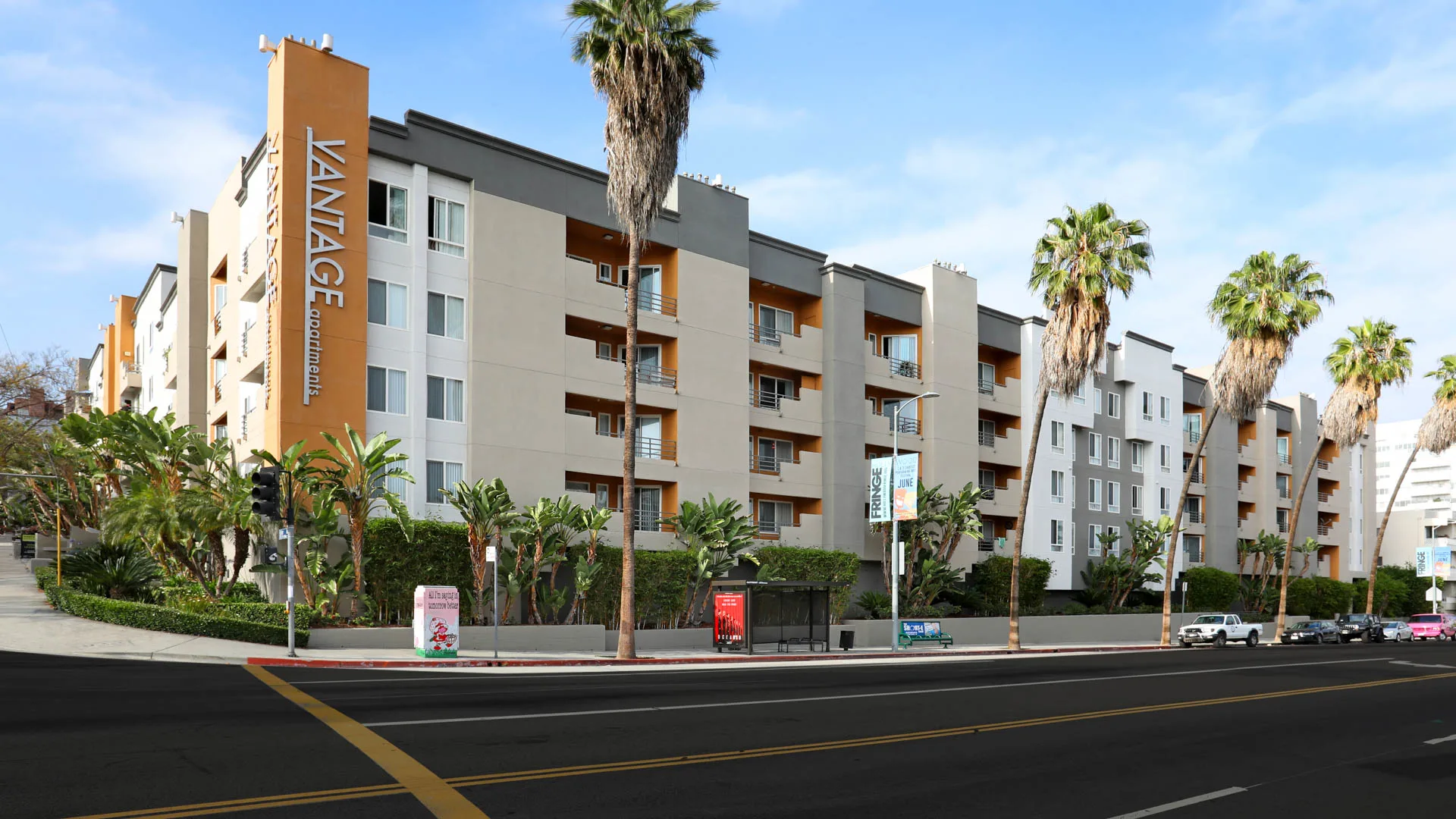 A multi-story apartment complex named Vantage Apartments with several palm trees in front, along with a bus stop and parked cars on the street.
