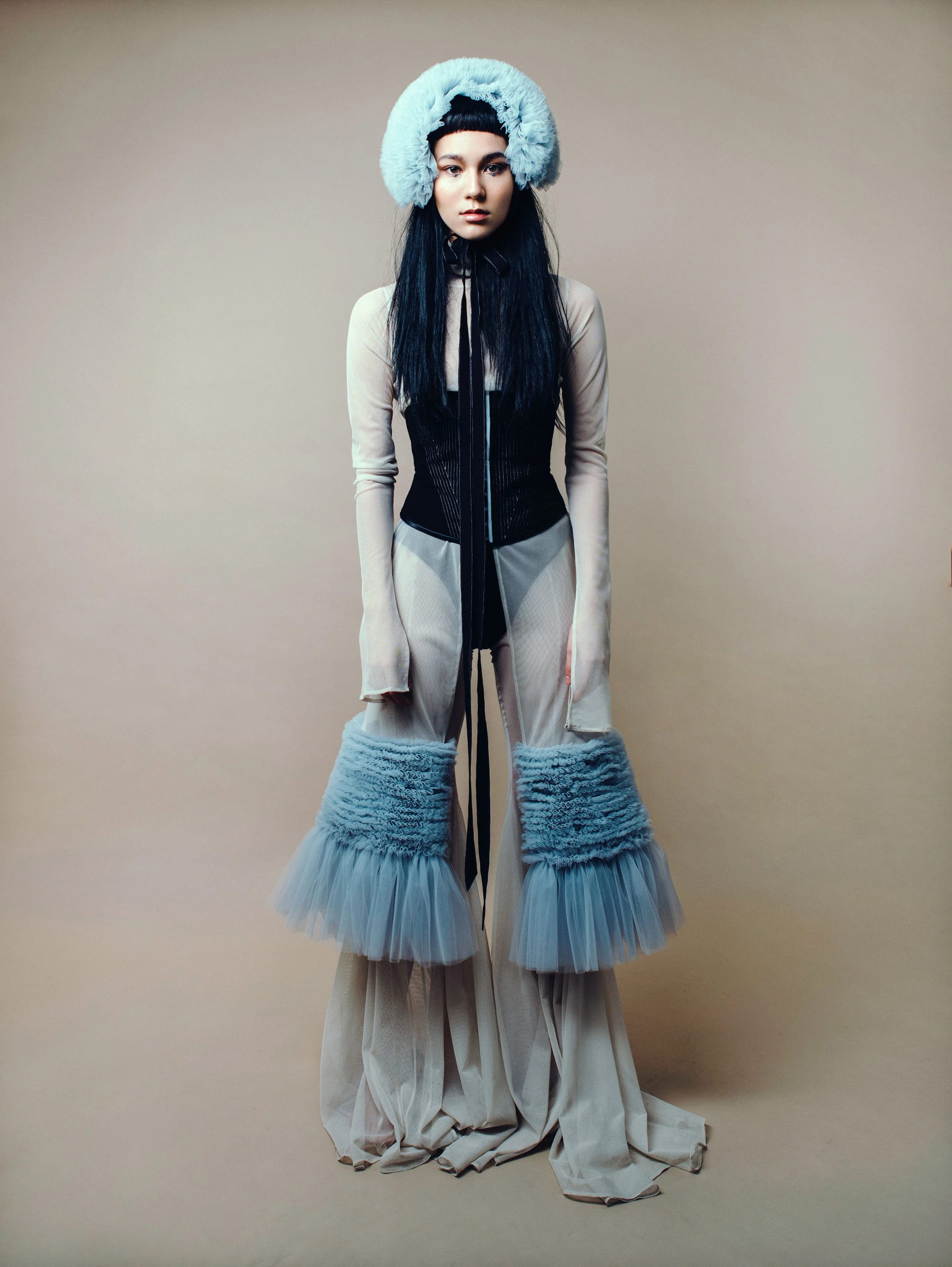  Wardrobe:  Blue ruffled tulle hat with black bands  Extremely flared mesh pants  Transparent dress with cut-out details and ruffled tulle  Black corsage with white stitches 