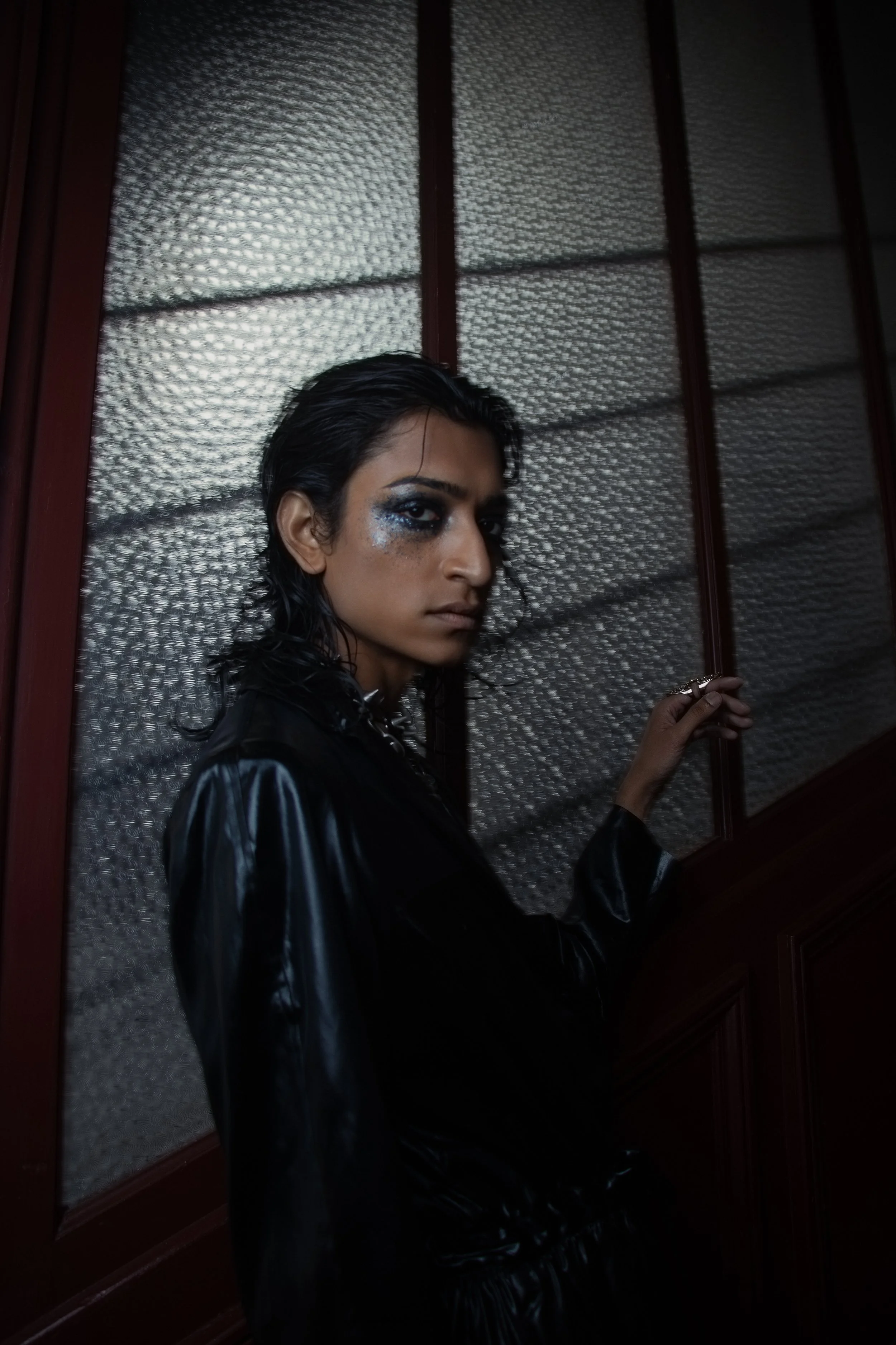 Wet hair, metallic shimmer, and dark leather create a cold, cinematic mood