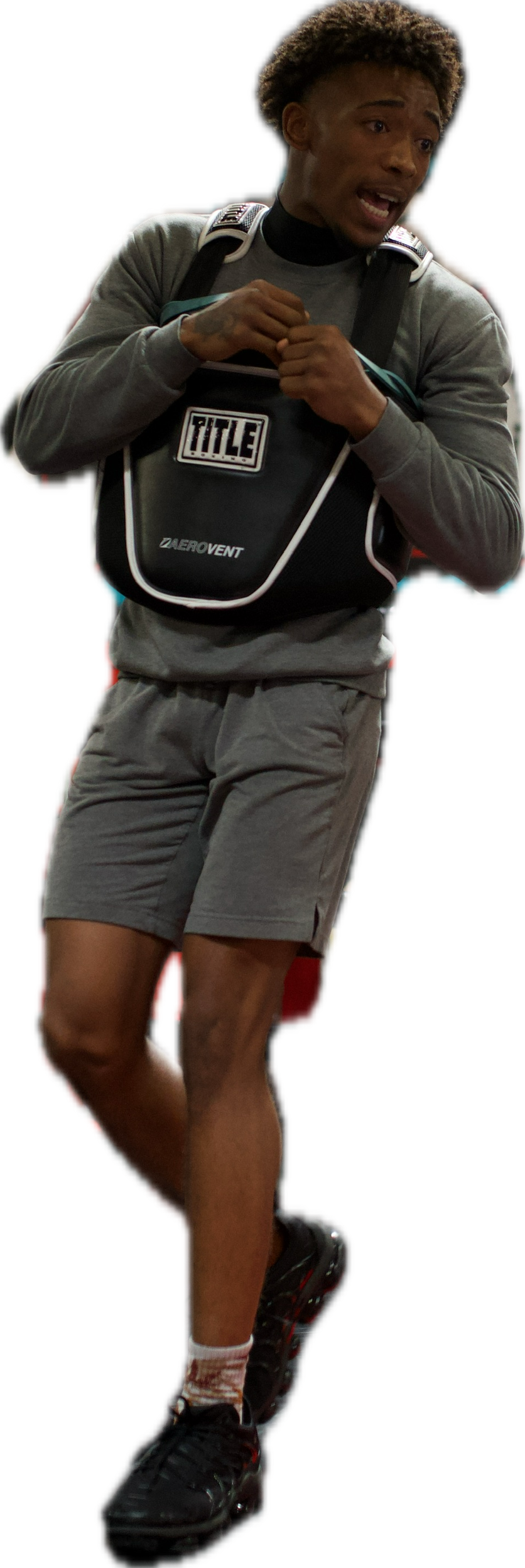 A young man dressed in athletic clothing, carrying a backpack, appears to be talking or explaining something.