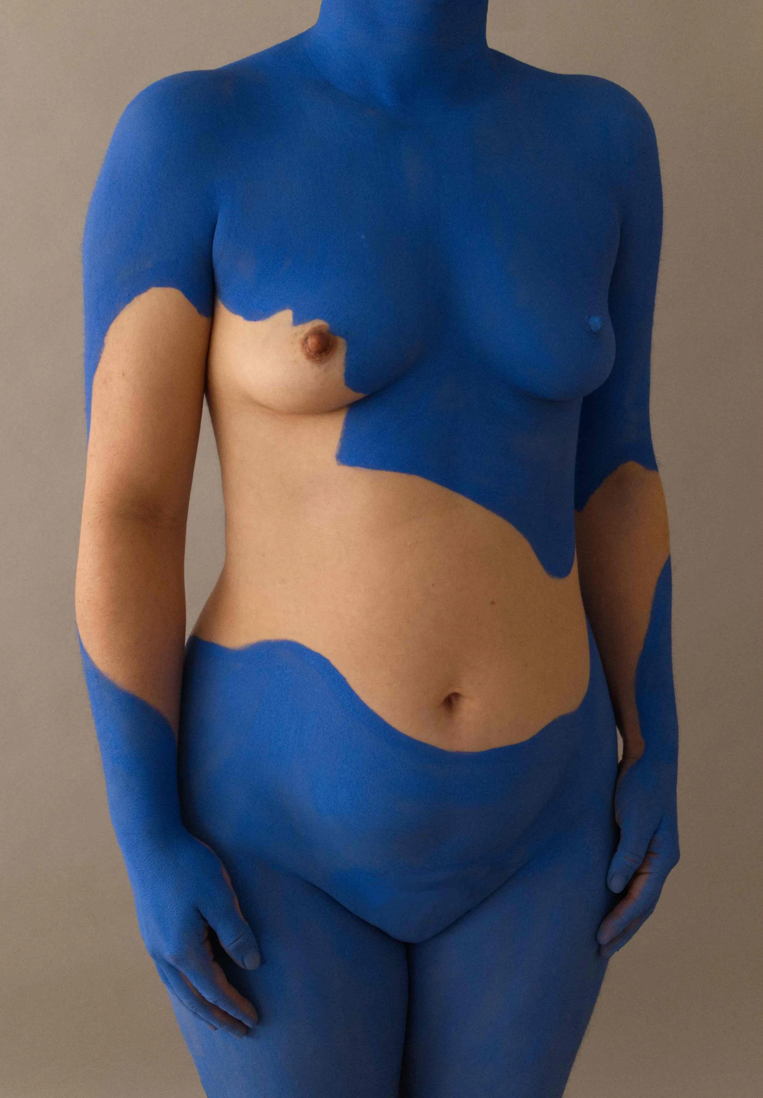 A woman with her skin painted in blue and nude colors, creating an abstract pattern that covers parts of her body, wearing blue gloves and no shirt.