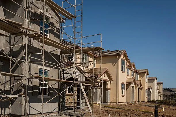 New residential houses under construction with scaffolding on the left side, in a suburban neighborhood on a clear day.