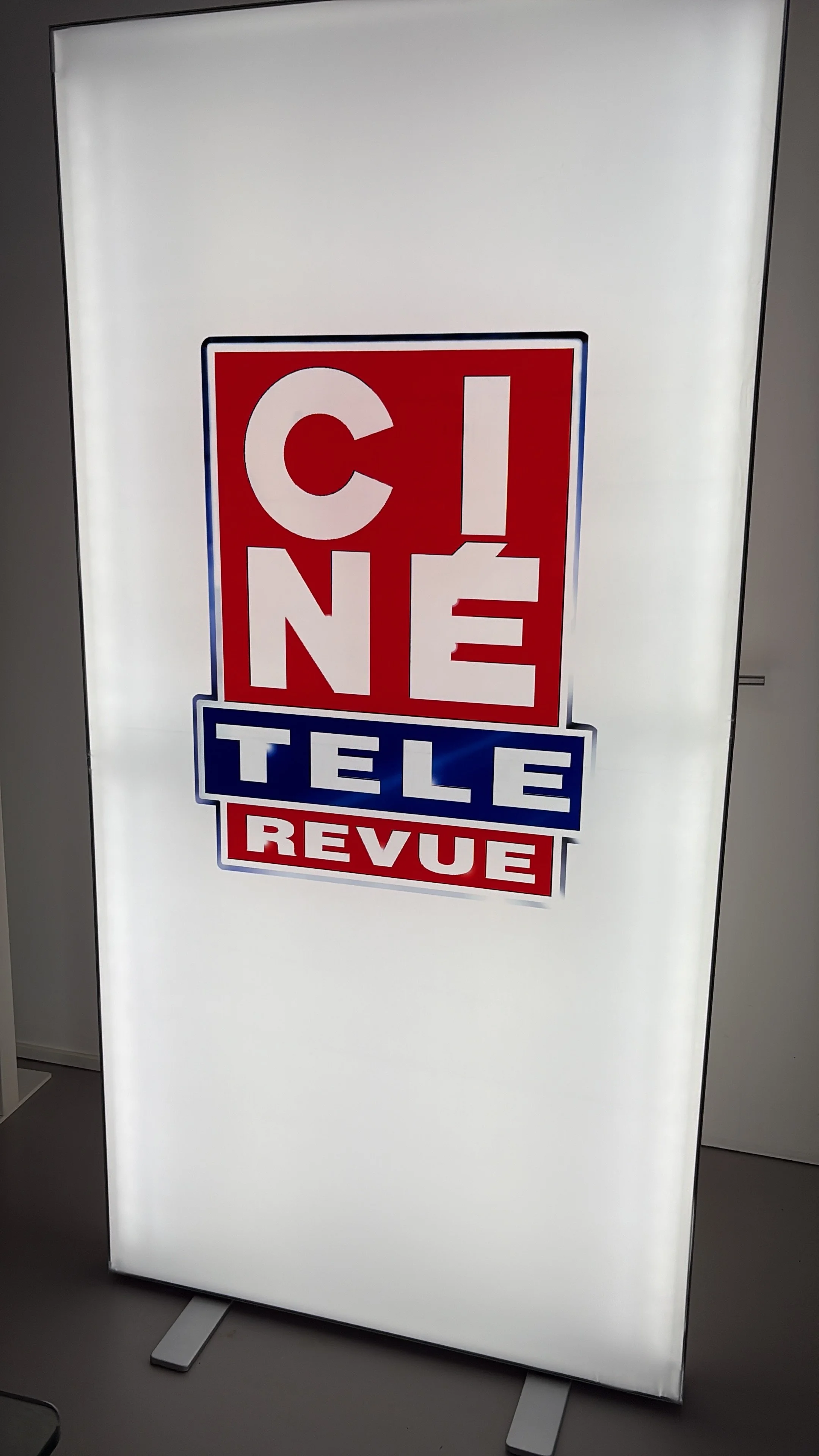 A vertical illuminated sign with the words 'COME', 'TELL', and 'REVEAL' in red, white, and blue colors.