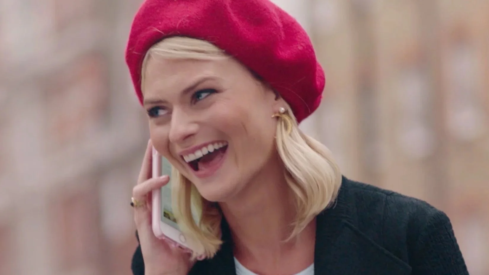 Woman with blonde hair, Pandora Sykes, talking on a pink cellphone, wearing a red beret and black blazer, smiling.