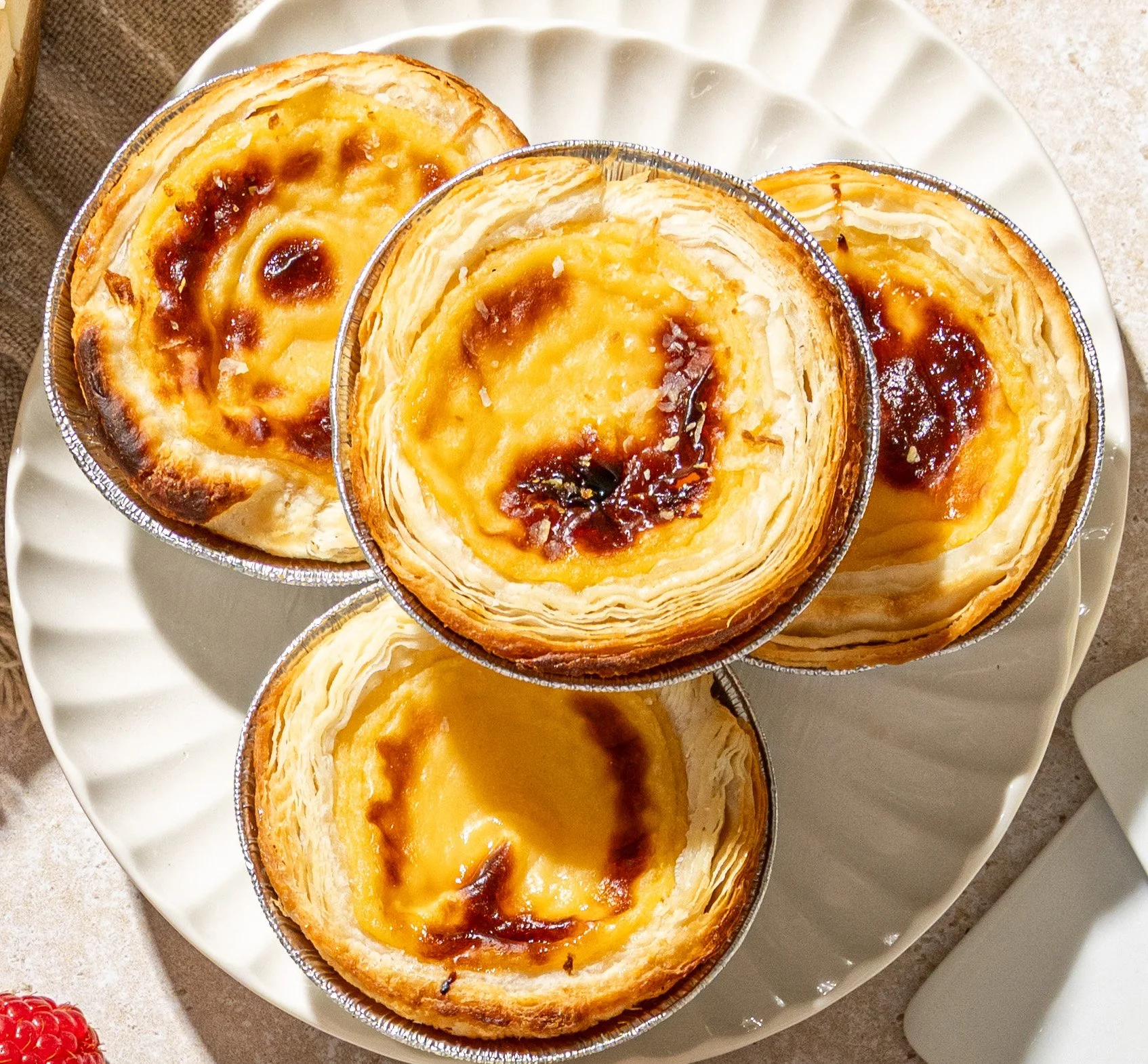 Four Portuguese egg tarts with flaky crust and custard filling on a white plate