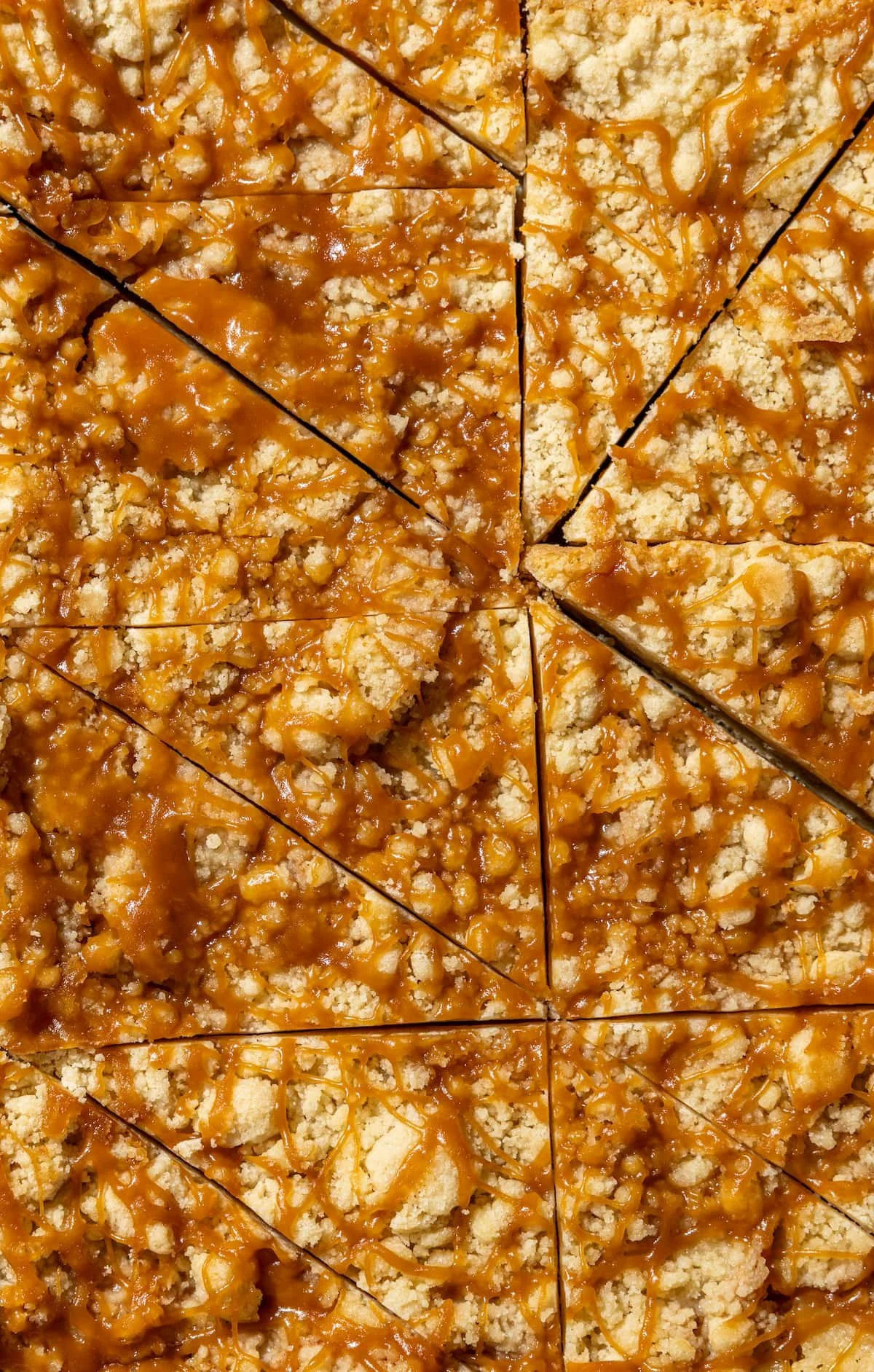 Close-up view of a caramel apple dessert cut into slices, with caramel sauce and crushed nuts on top.