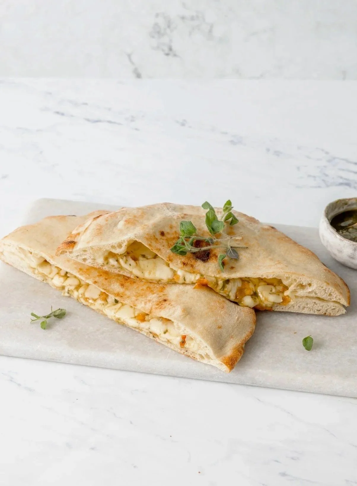 Pizza sandwich with cheese, herbs, and vegetables, served with a side of dipping sauce.