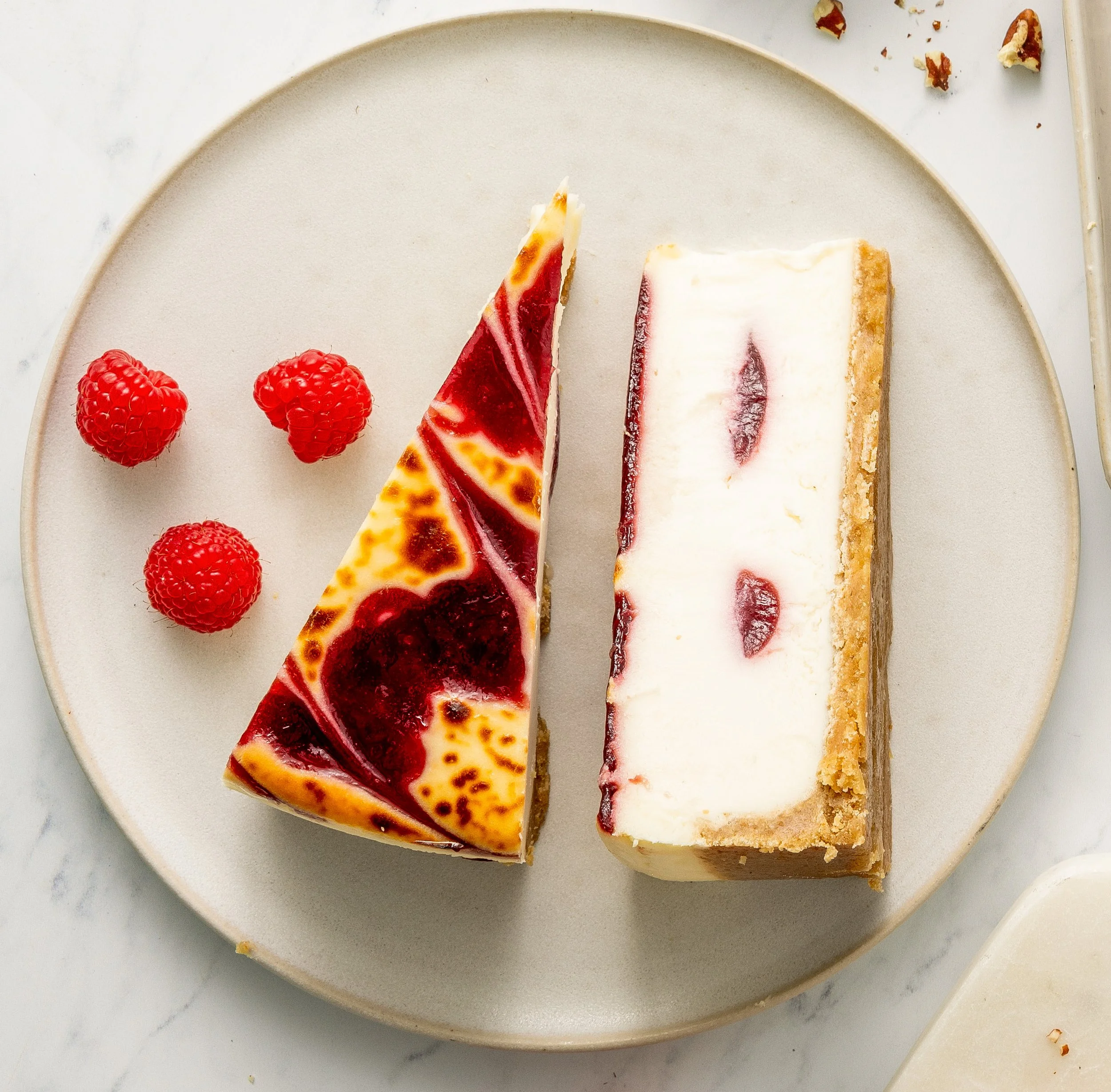 Two slices of cheesecake topped with raspberry sauce and three fresh raspberries on a white plate.