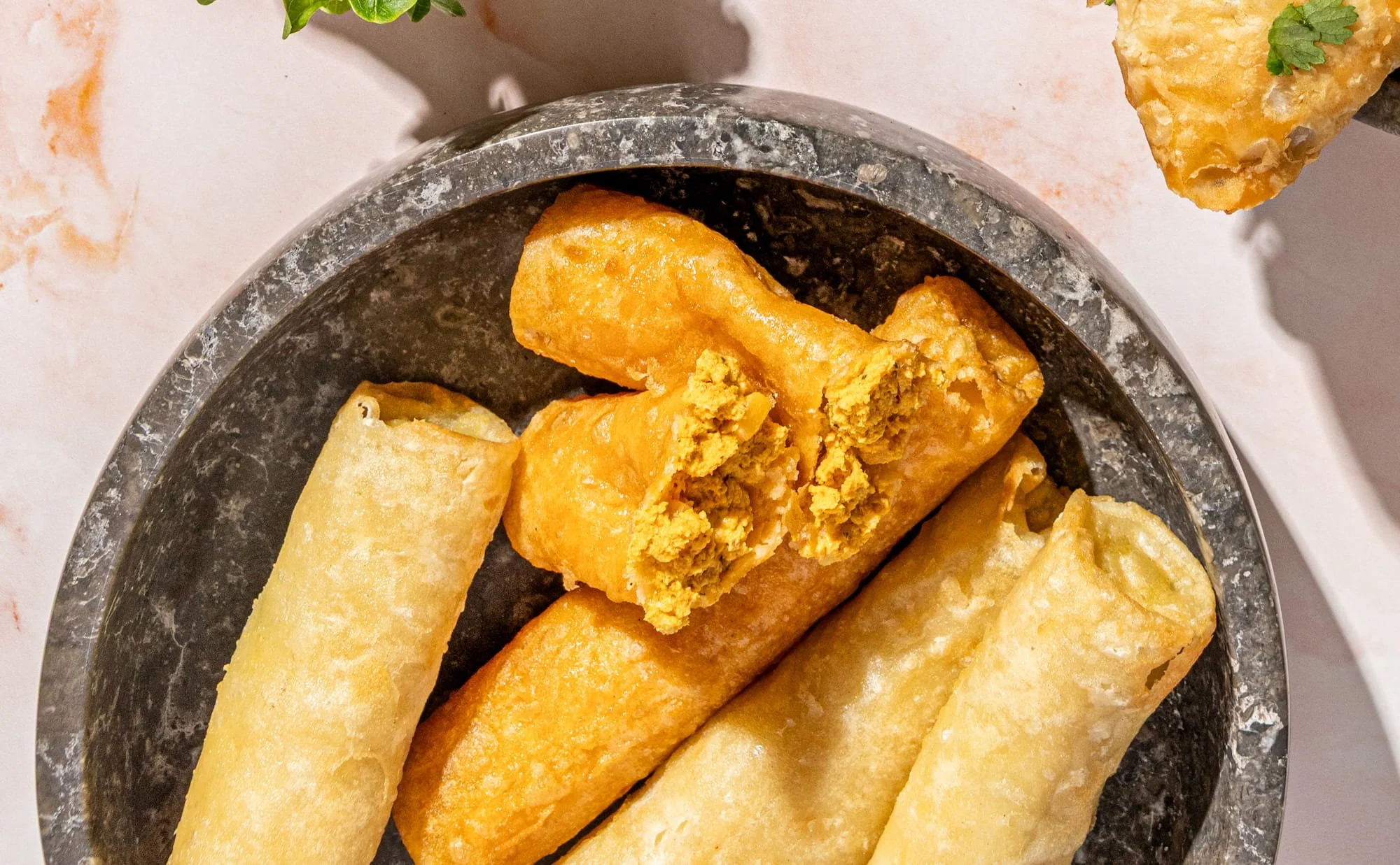 Close-up of golden-fried taquitos on a stone serving plate, with one taquito broken open showing its delicious filling.