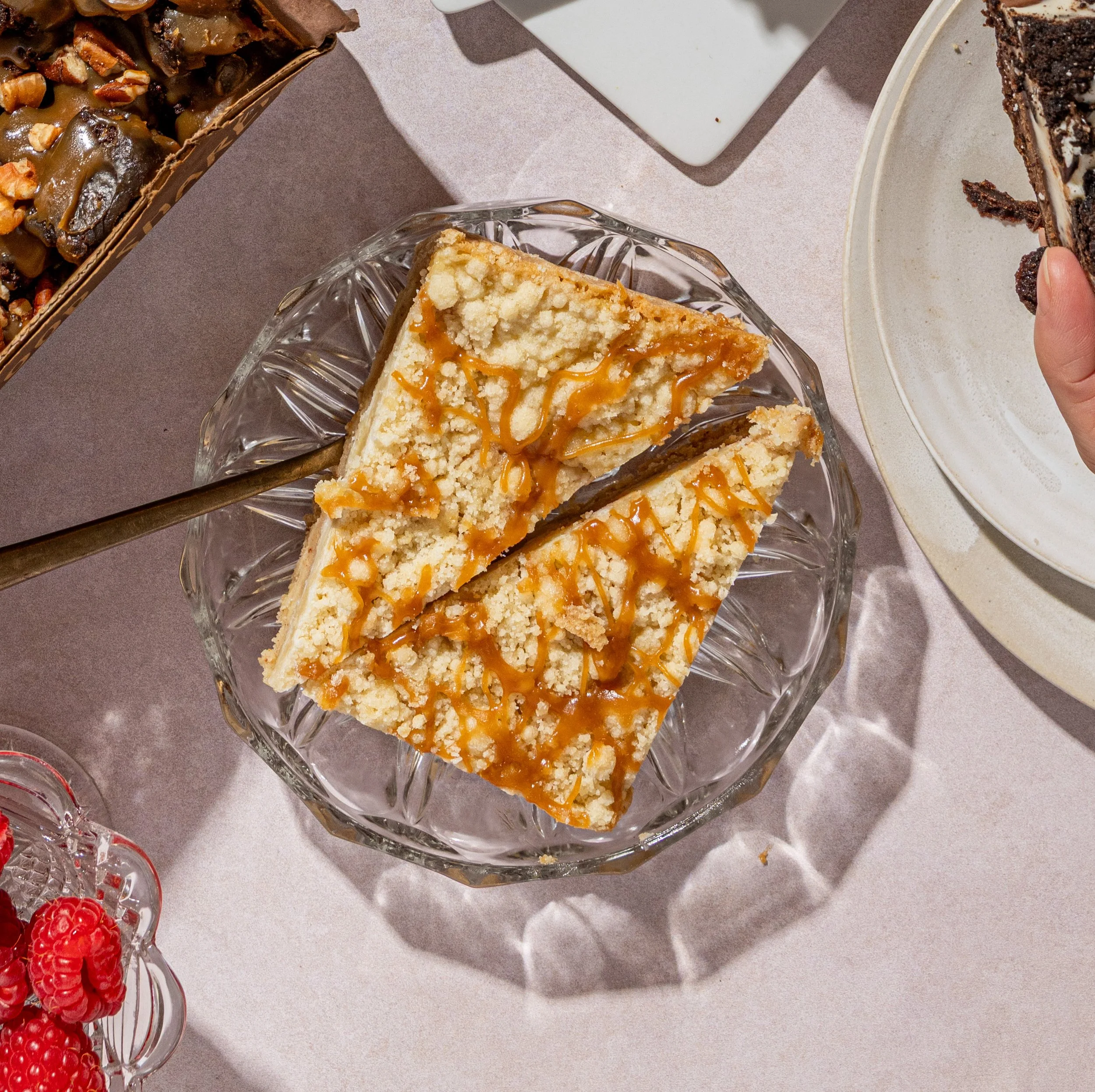 A slice of apple with caramel drizzle on a glass plate surrounded by assorted desserts.