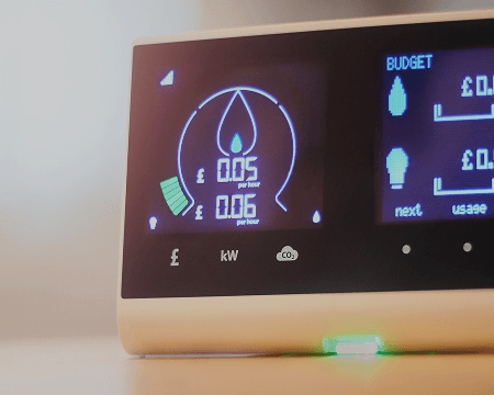 An energy monitor displaying power consumption, with a needle indicating low usage, and a digital screen showing budget and energy details.