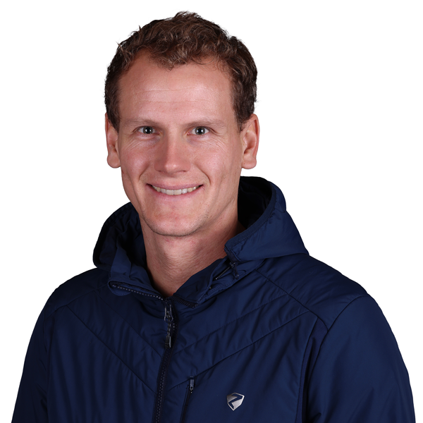 Hannes Lechner mit kurzen, lockigen braunen Haaren, blauen Augen und einem Lächeln trägt eine dunkelblaue Skijacke vor weißem Hintergrund.